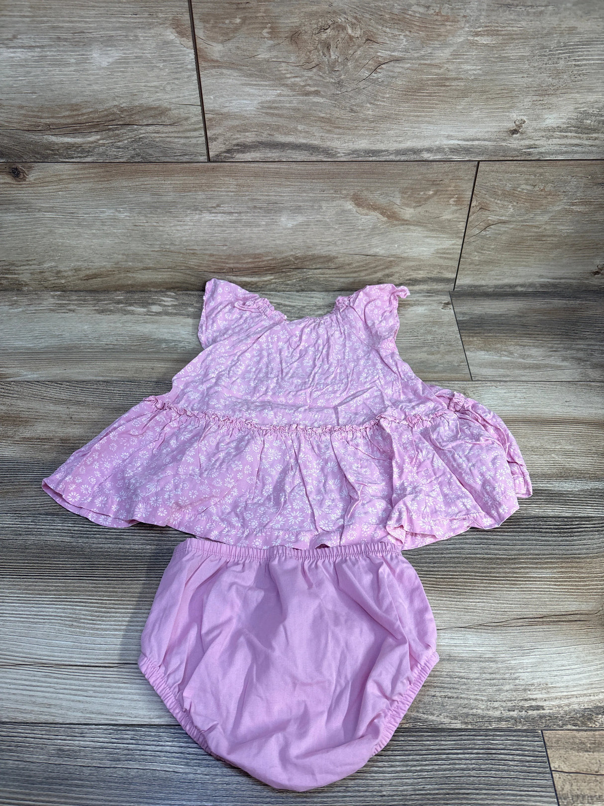 Flat-lay of Carter's pink floral dress with matching bloomers, flutter sleeves and elastic waist on wood floor