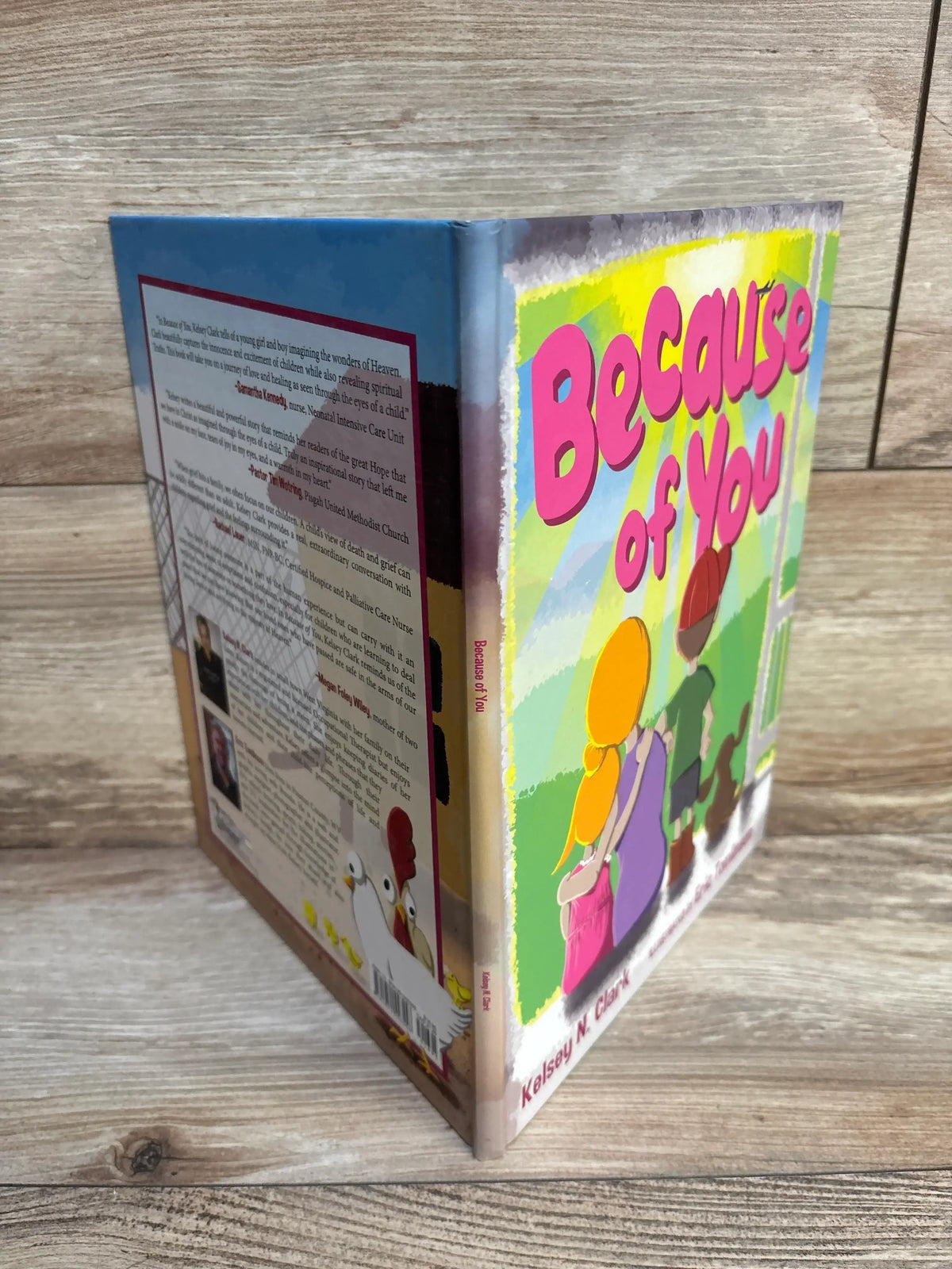 Angled view of Because of You hardcover children's book showing illustrated front and back covers on wood background