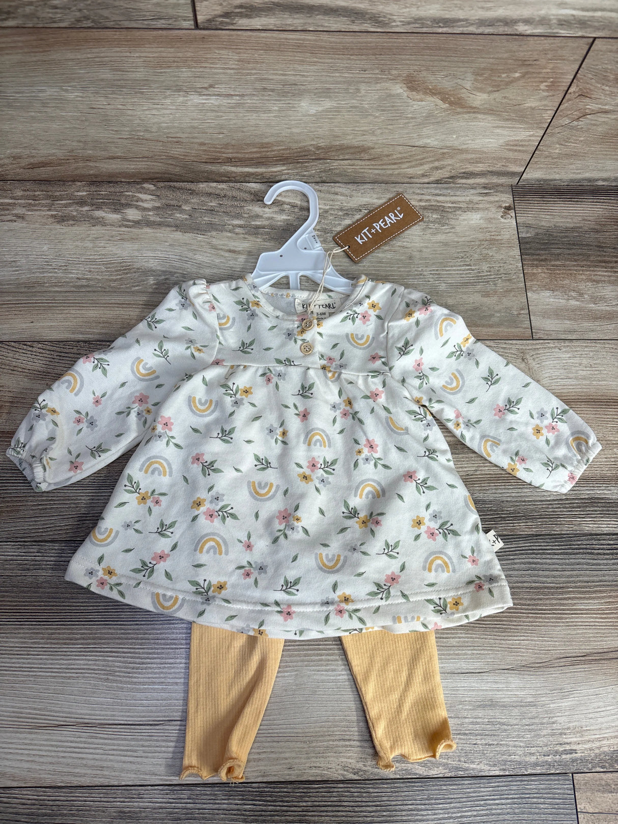 Baby girl outfit with floral and rainbow print dress by Kit+Pearl and mustard leggings on wooden floor