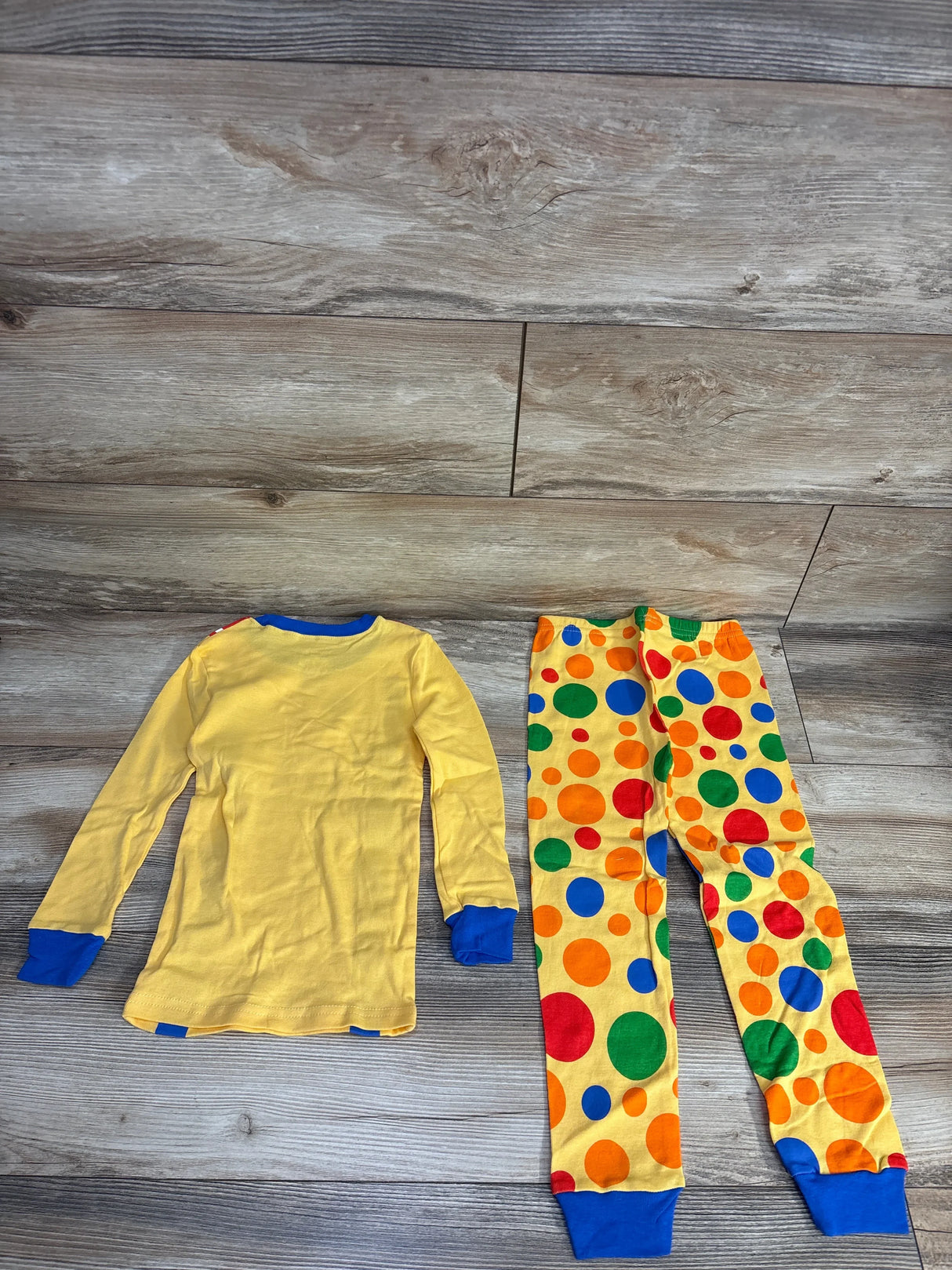 Yellow kids pajamas with blue cuffs and colorful polka dot pants on wood floor