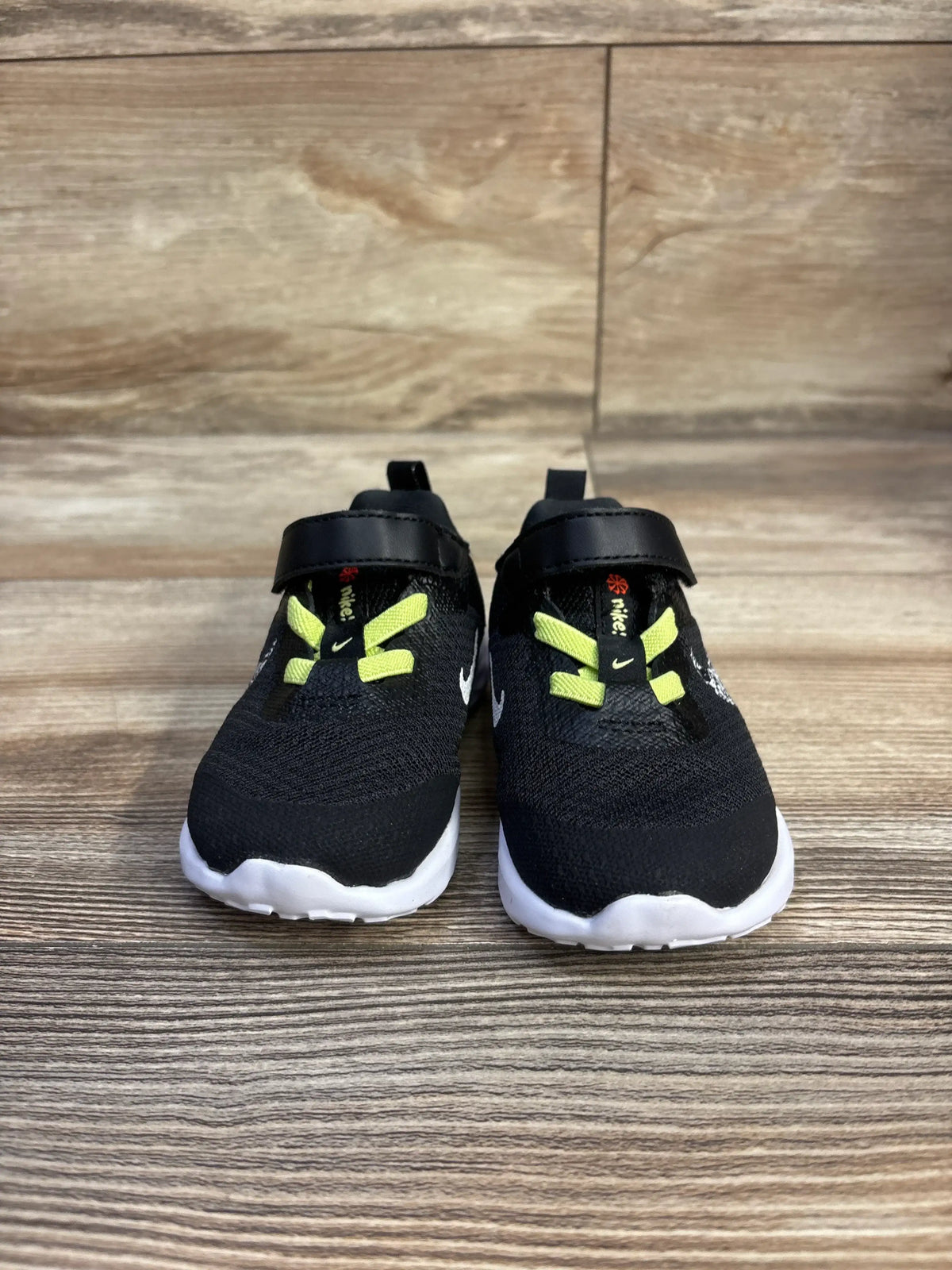 Front view of Nike Revolution 6 toddler sneakers size 4C, black with neon yellow laces and velcro strap on wood background
