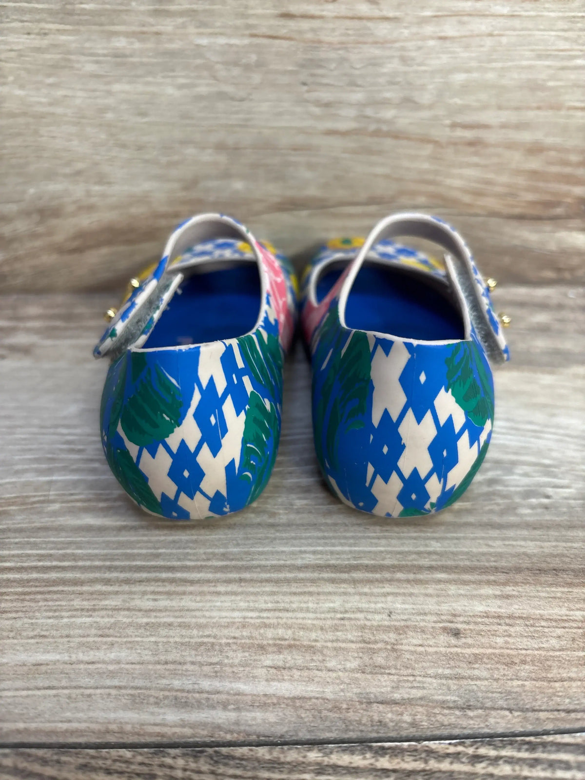 Rear view of Vivienne Westwood x Melissa Mary-Jane shoes in blue-green geometric print with gold strap studs on wood