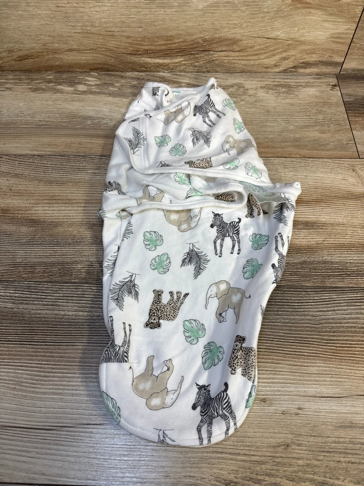 Baby swaddle blanket with safari animal print, elephants, zebras, and leaves on wood floor