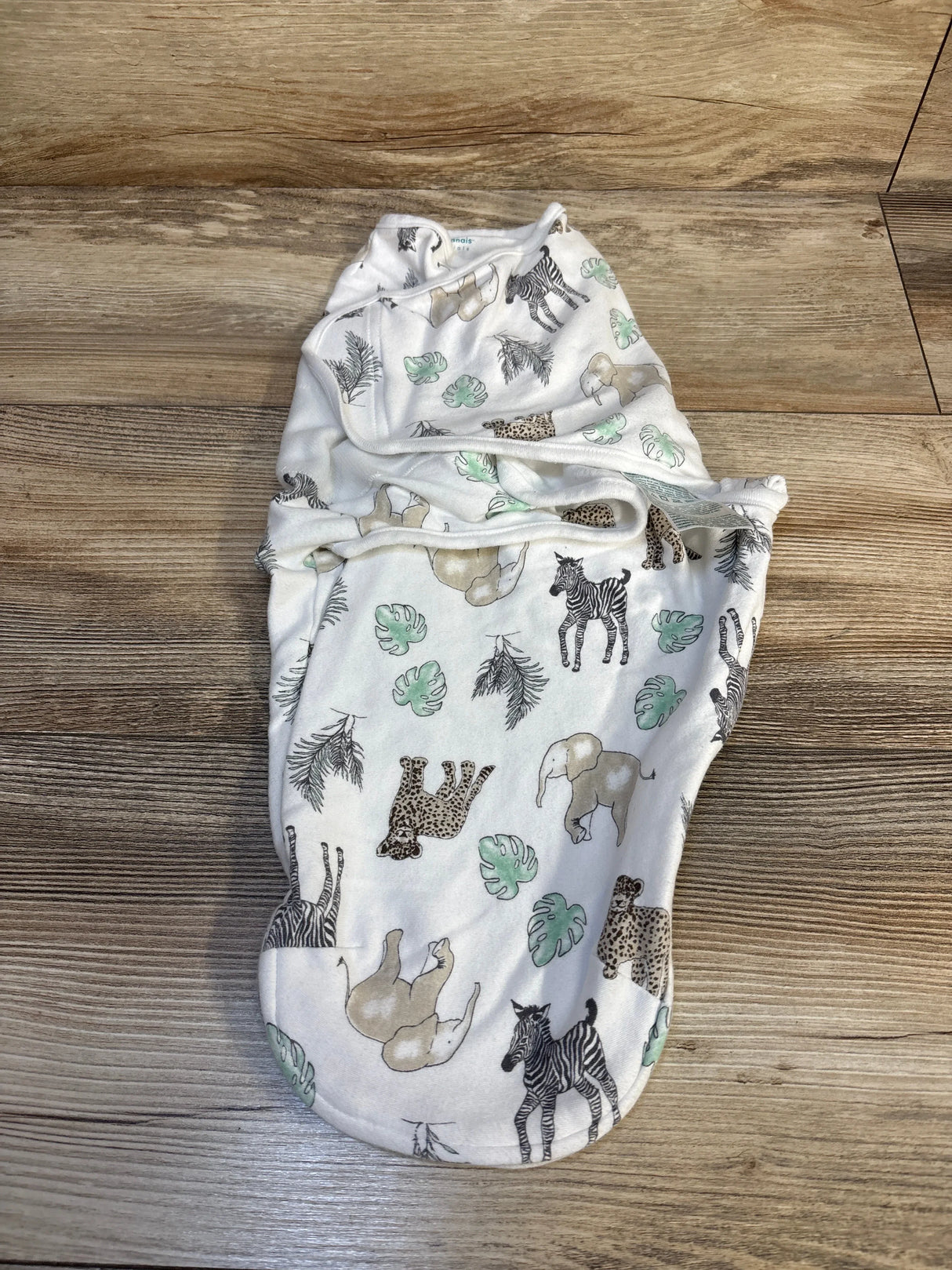 Baby swaddle blanket with safari animal print, elephants, zebras, and leaves on wood floor