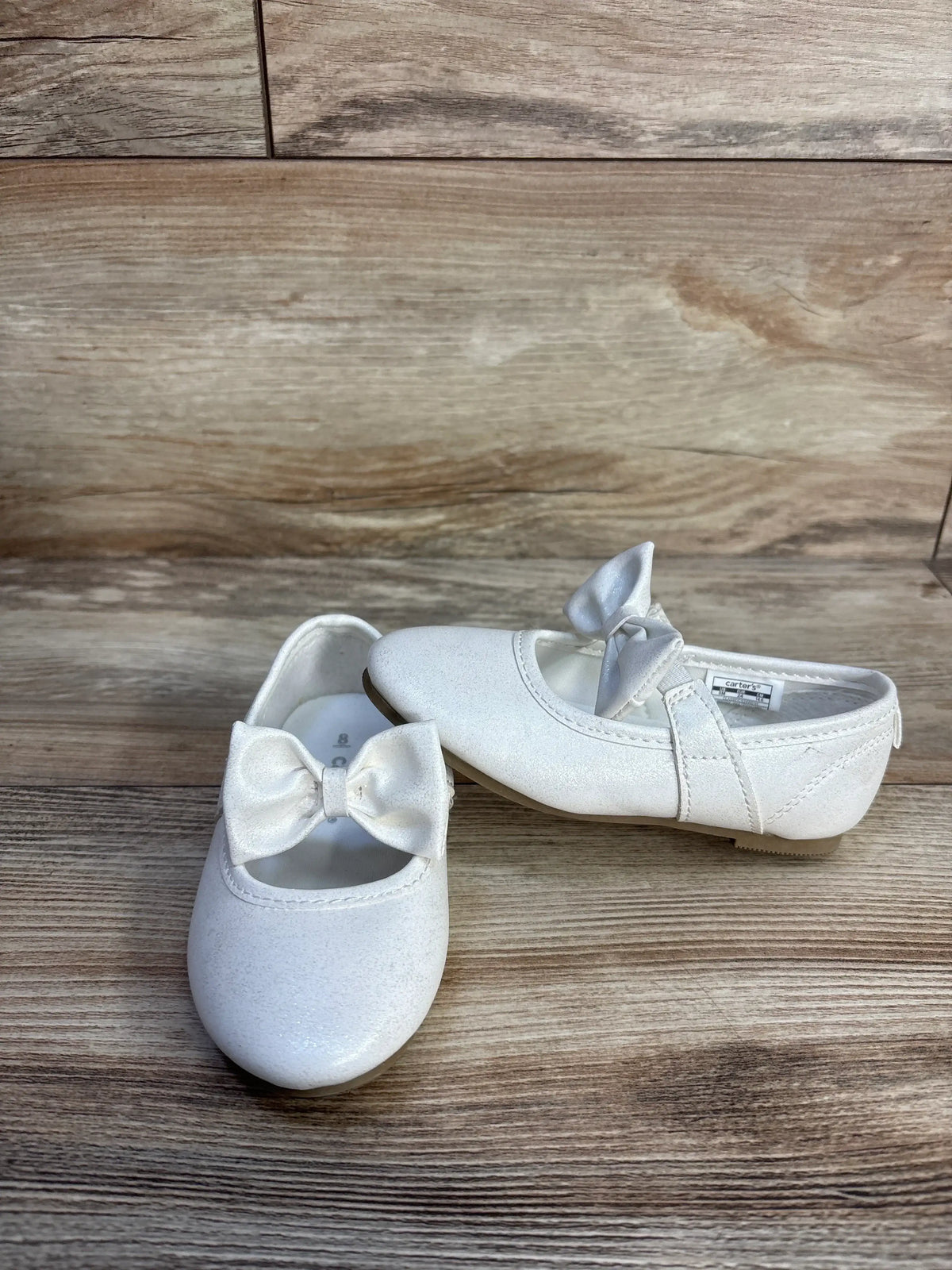 Pair of white Carter's classy Mary Jane flats with bows for girls on a wooden background.