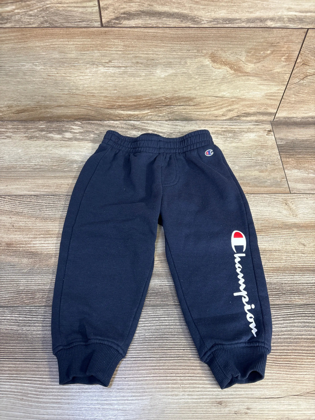 Front view of Champion navy joggers for 18 months showcasing logo, elastic waistband, and ribbed cuffs on a wood-look floor