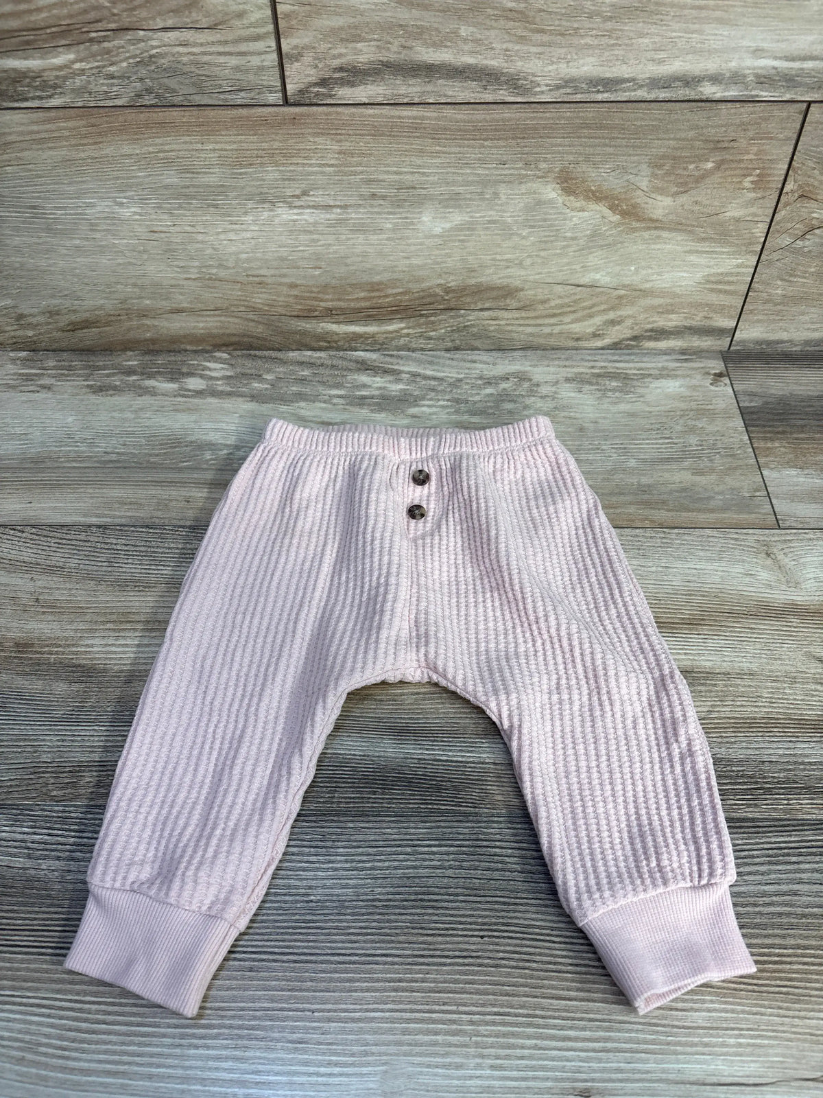 Top-down view of pink thermal baby joggers, waffle texture, two buttons, elastic waist and ribbed cuffs on wood floor