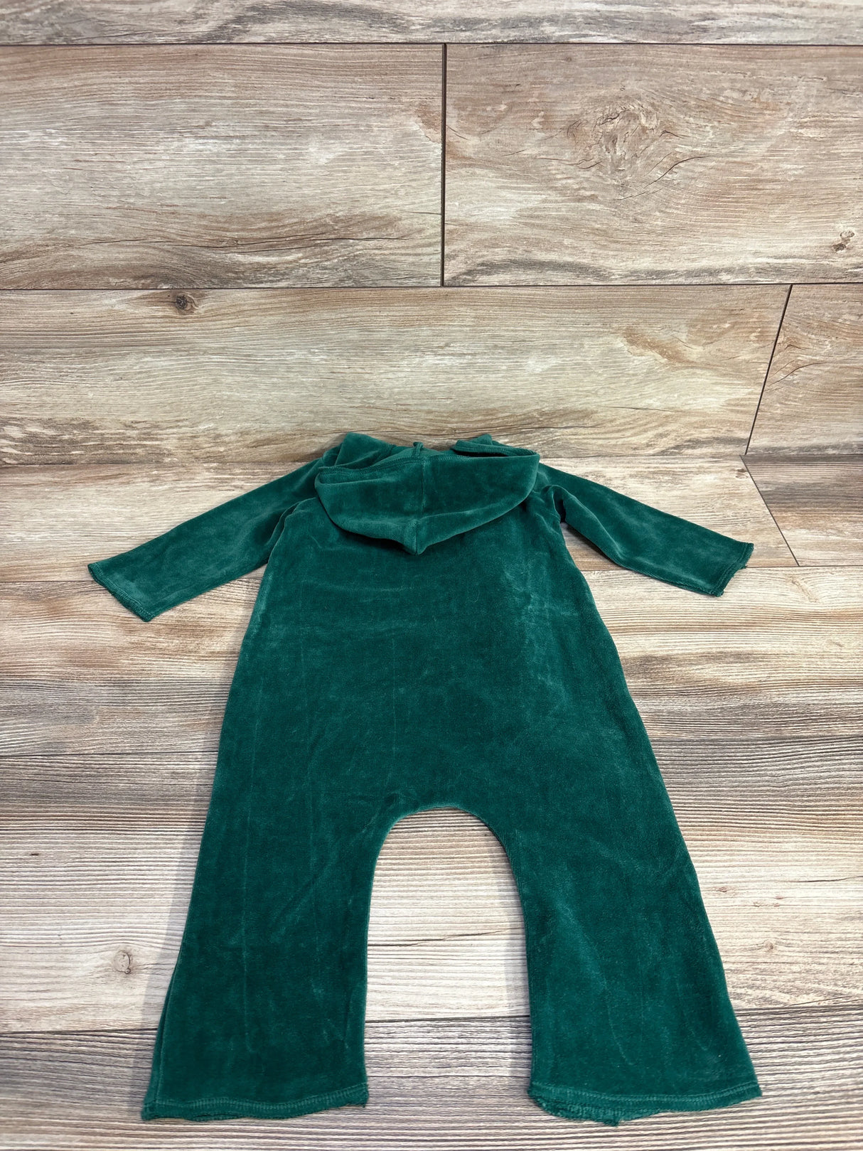 Green velvet baby onesie with hood laid flat on wooden floor
