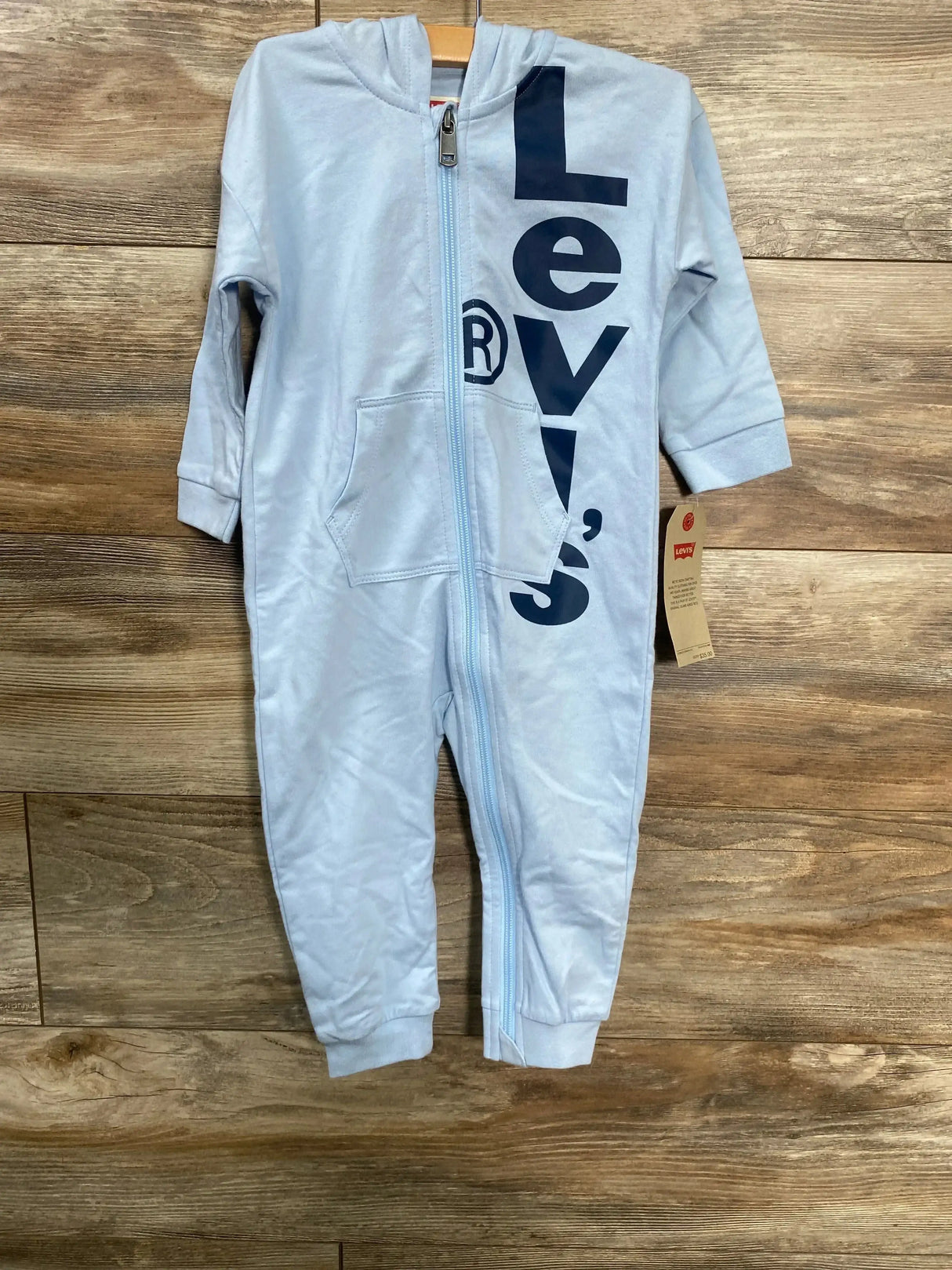 Front of light blue Levi's hooded baby coverall size 18m with full zipper, kangaroo pocket and vertical navy logo on wood