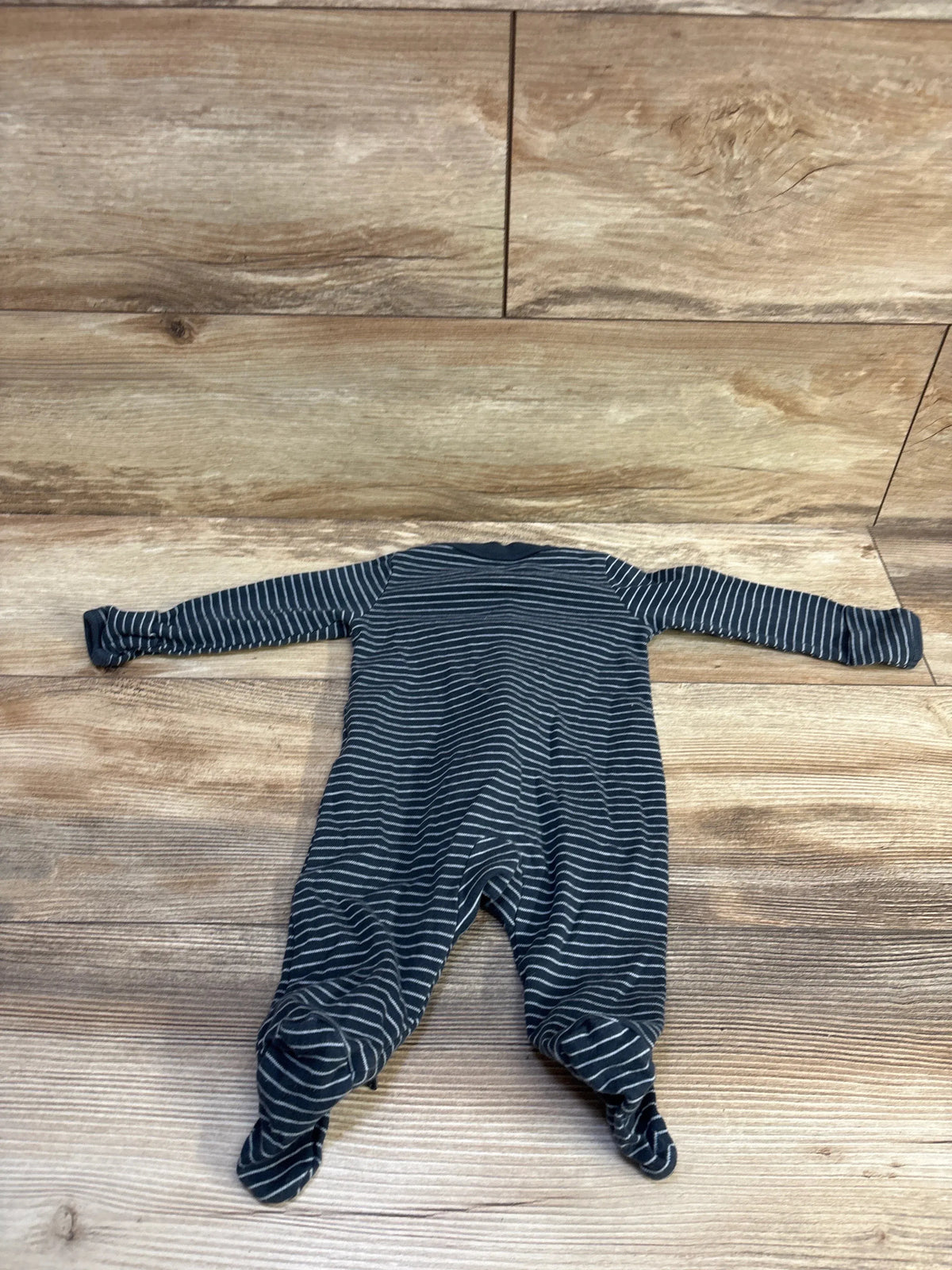 Flat lay of Carter’s footed sleeper showcasing navy blue fabric with thin white stripes and built-in feet, size 3 months, on wood floor