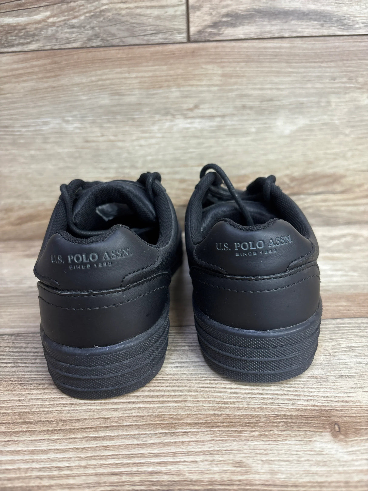 Back view of black U.S. Polo Assn. kids' sneakers on wood floor
