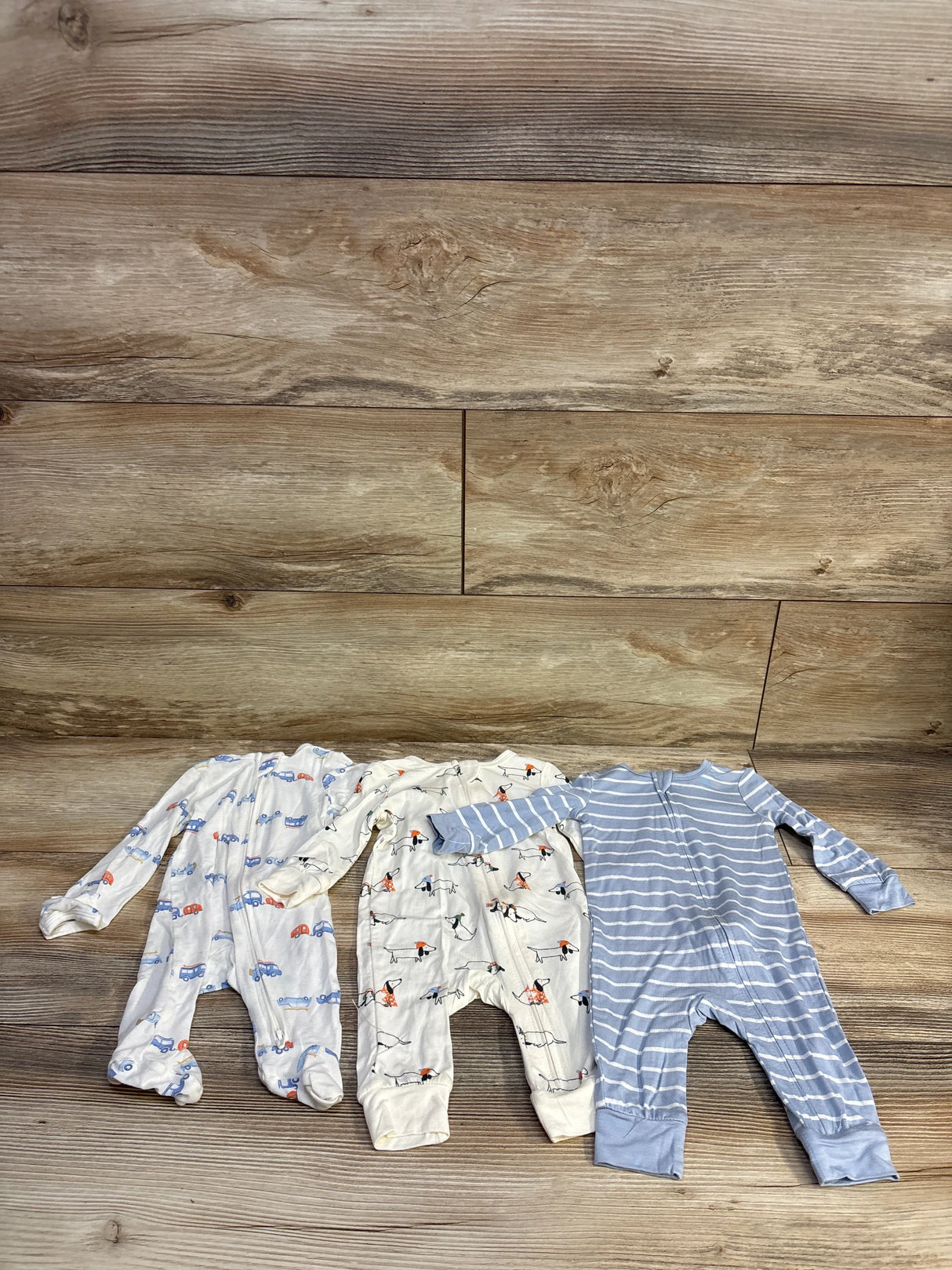 Flat lay of three Little Me bamboo footless sleepers 3 month showcasing ivory and patterned prints on wood floor background