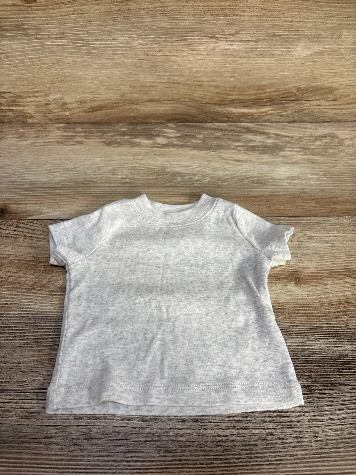 Front view of Just One You newborn shirt showcasing its soft grey color and crew neckline on a wood-grain background