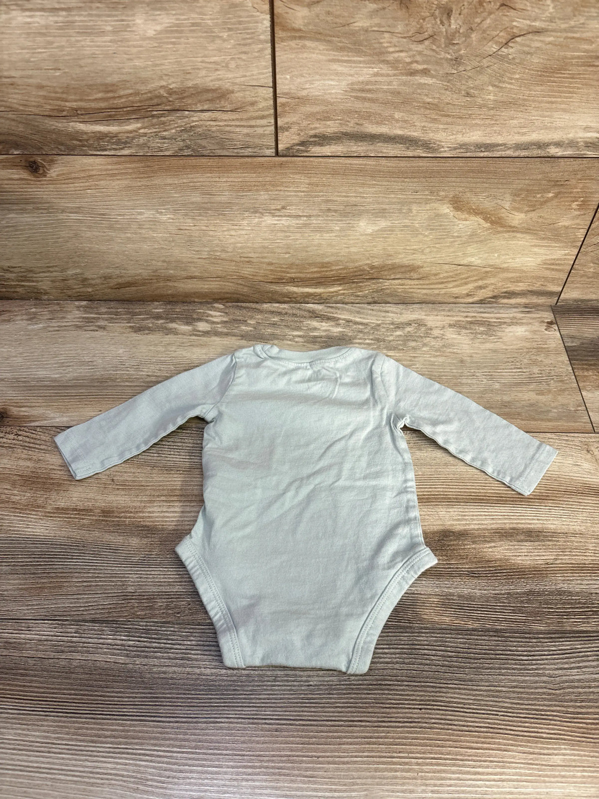 Top-down view of Carter’s Poppin’ Bottles bodysuit showcasing its green long-sleeve design on a wood-look background