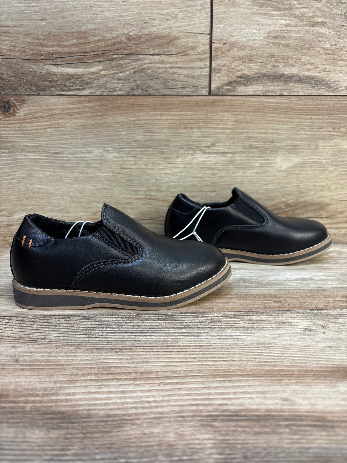 Black slip-on boys dress shoes with tan soles on wood background