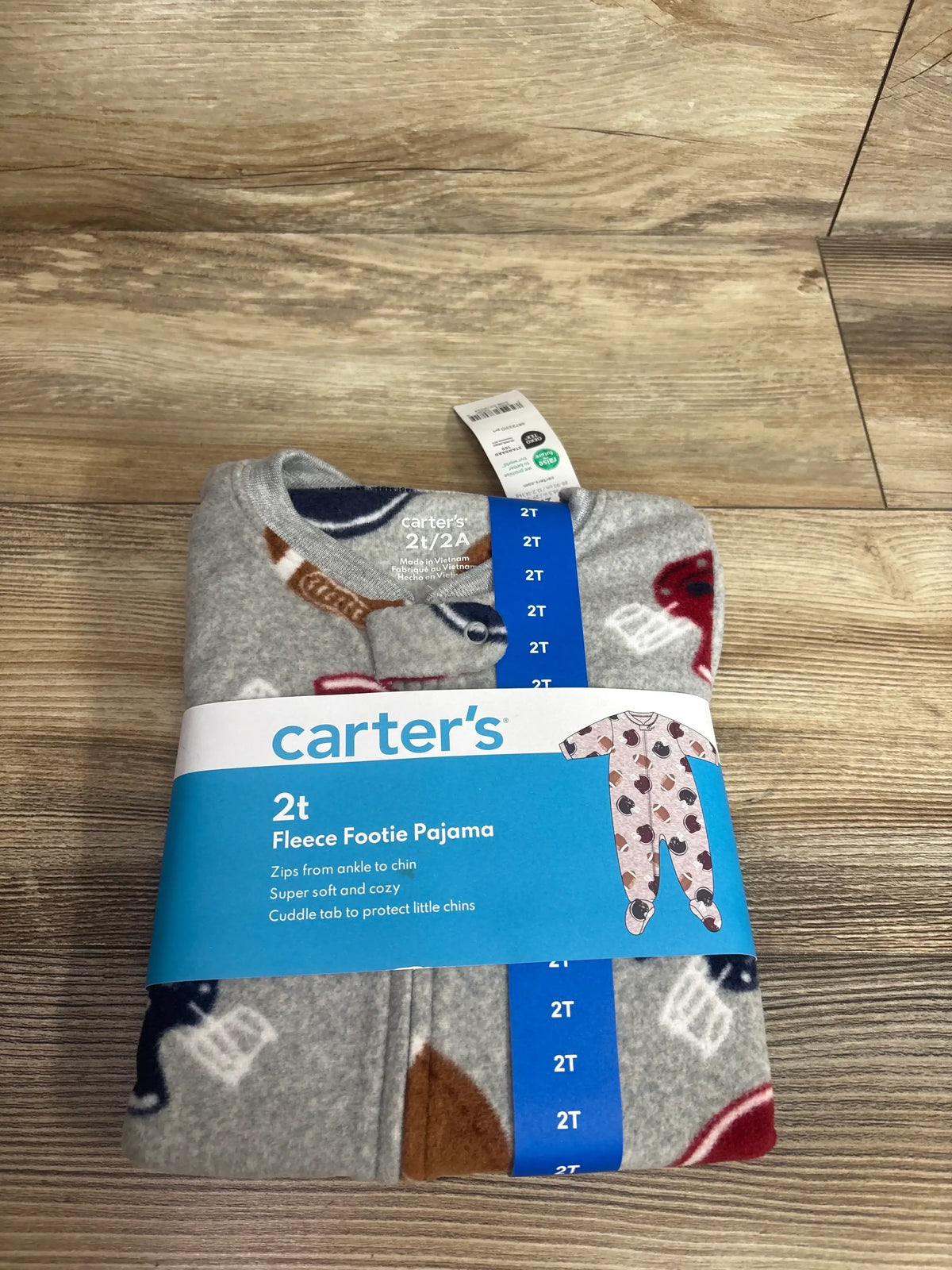 Folded front view of Carter’s grey fleece 2T footie pajama showcasing football and helmet print and blue size band on wood floor