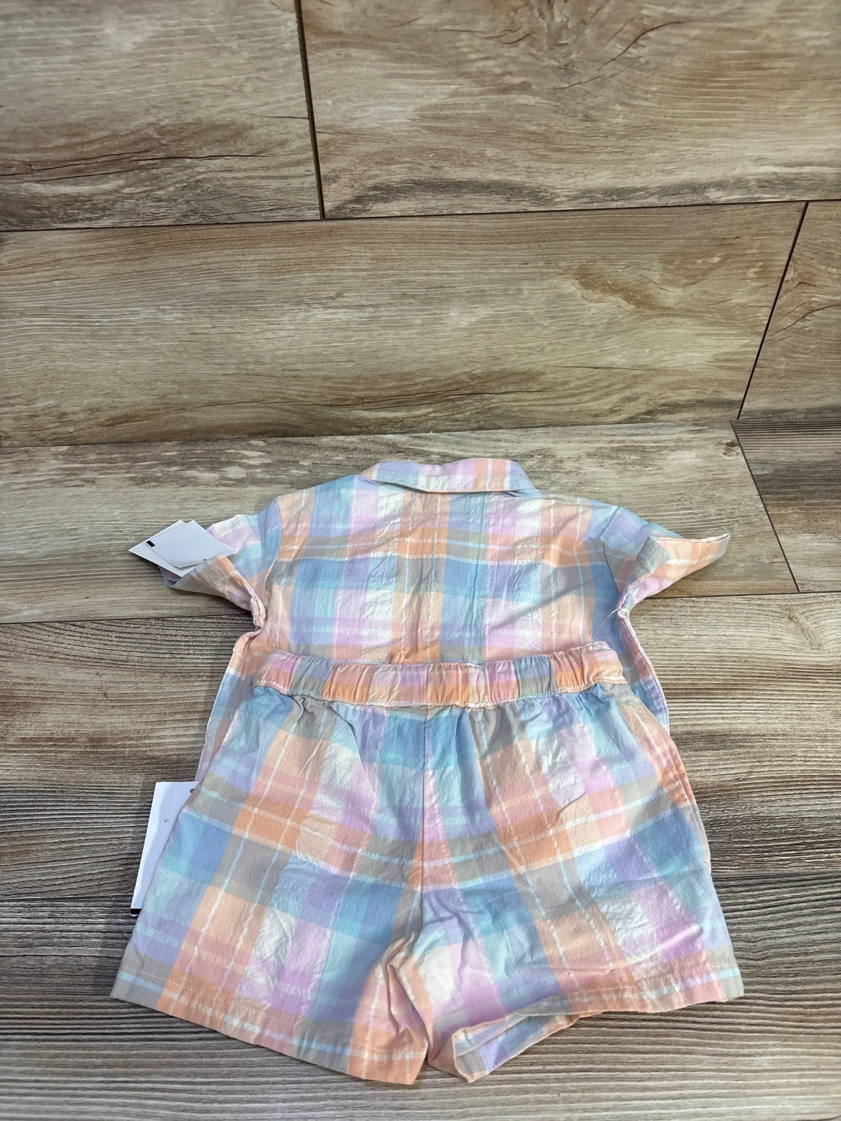 Back flat-lay of toddler two-piece coral pastel plaid shirt and elastic-waist shorts on wood background