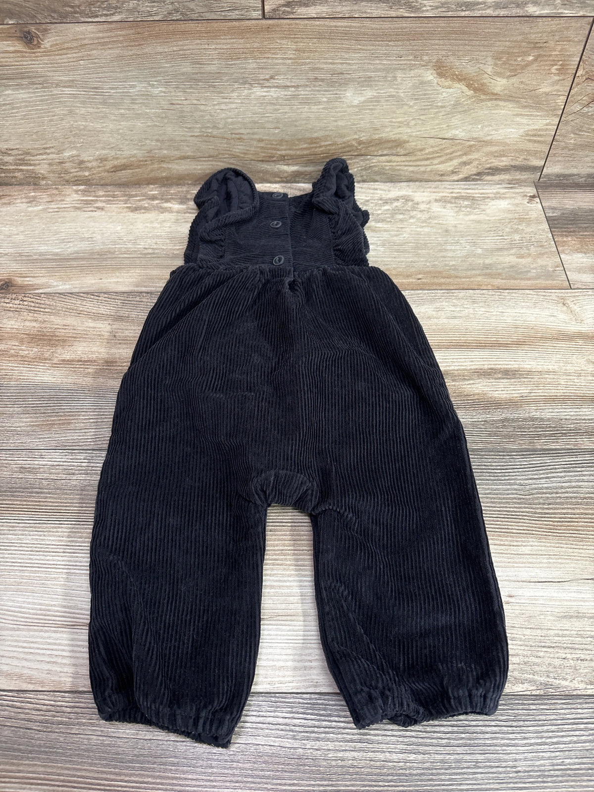 Baby Gap black corduroy ruffle overalls for infants size 6-12m on a wooden background