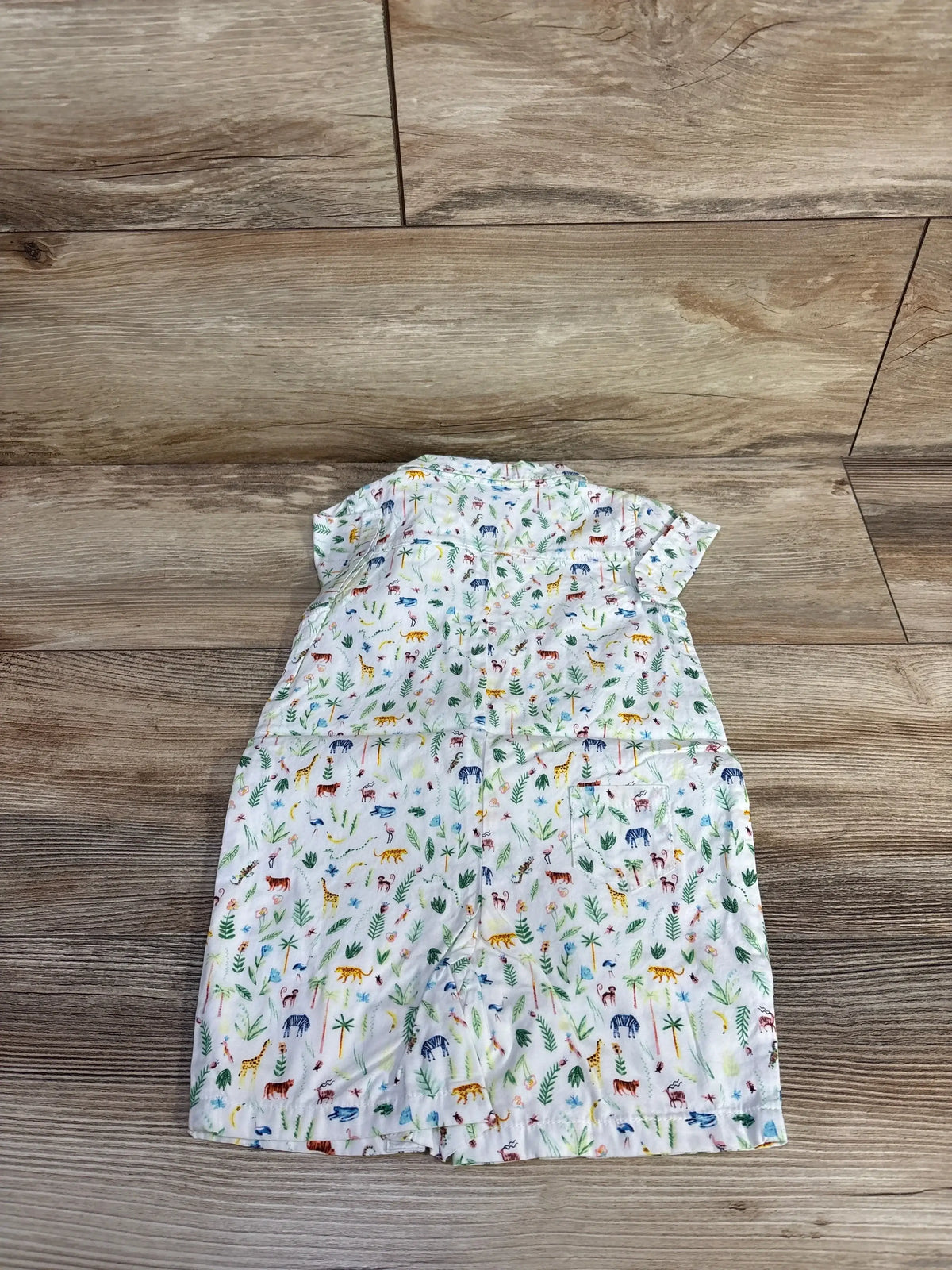 Flat lay of new Janie and Jack shortie romper size 6-12m in white with colorful jungle animal and palm print on wood plank floor