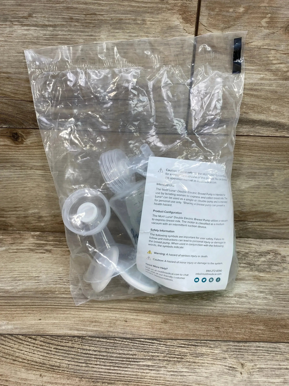 Top-down view of Motif Luna 24mm resupply kit showing breast pump replacement parts in a clear plastic bag on a wood surface