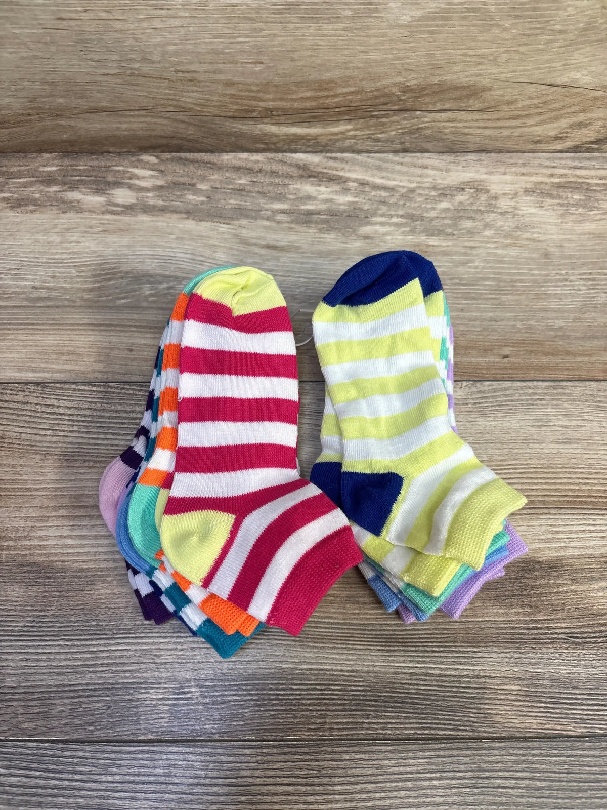 Top-down view of nine-pack baby ankle socks showcasing colorful stripes and contrasting heels with wood-grain background