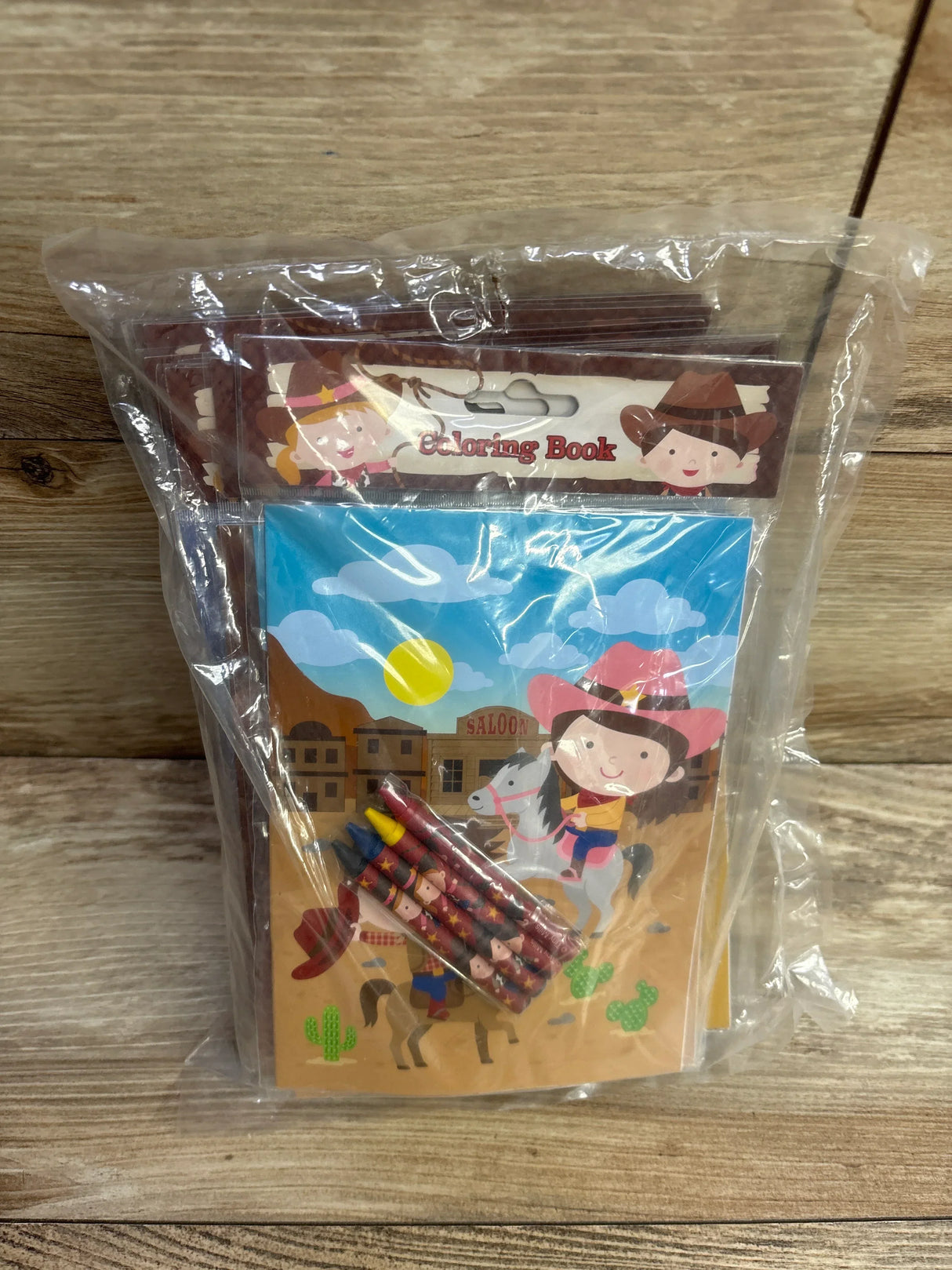 Children's cowboy-themed coloring book kit with crayons in clear packaging on wood background
