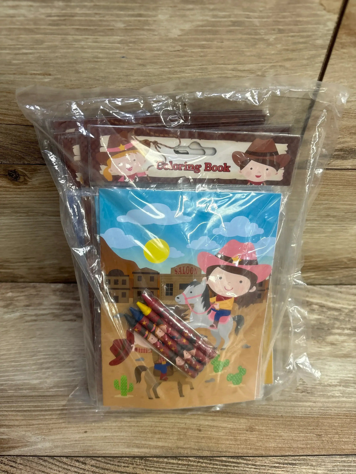 Children's cowboy-themed coloring book kit with crayons in clear packaging on wood background