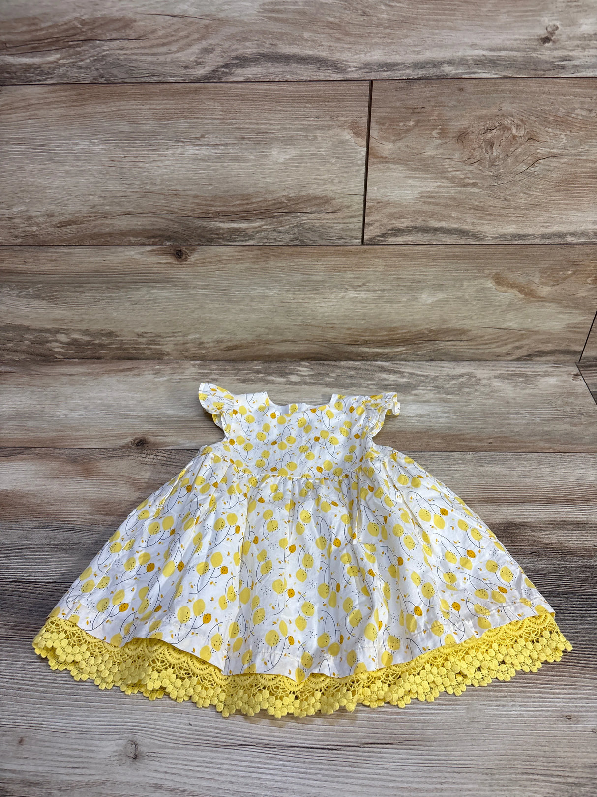 Flat lay of Du Pareil Au Meme lemon-print dress size 12M with flutter sleeves and yellow crochet hem on wood background