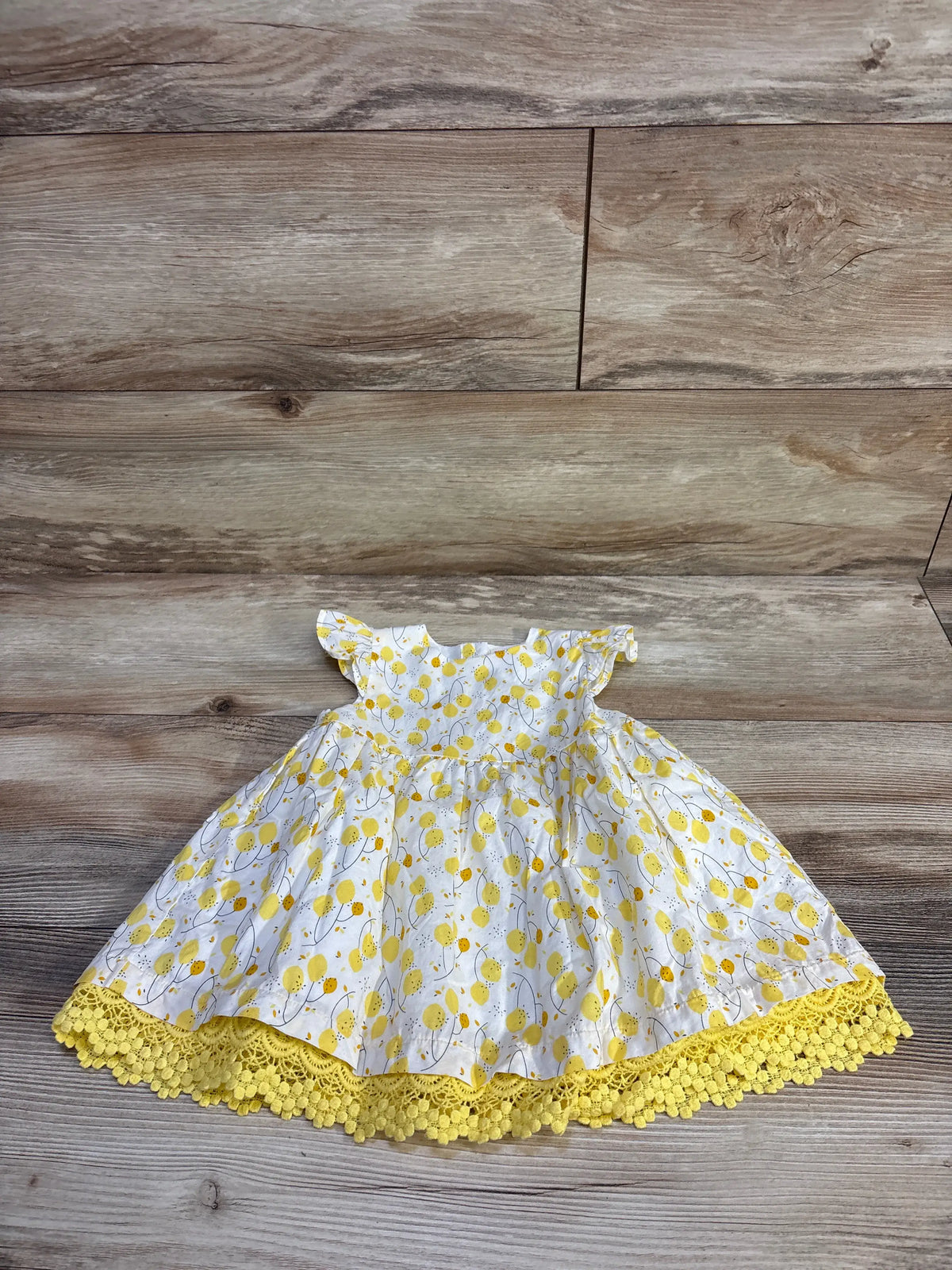 Flat lay of Du Pareil Au Meme lemon-print dress size 12M with flutter sleeves and yellow crochet hem on wood background