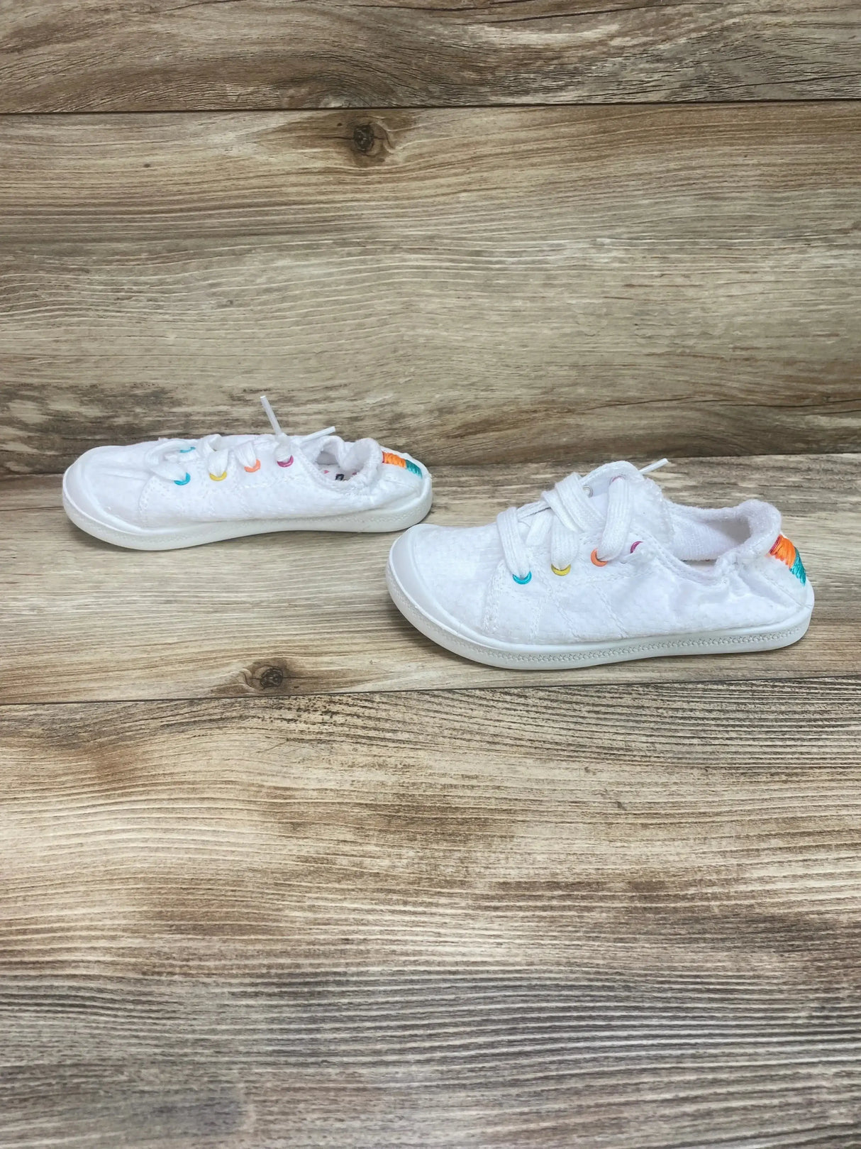 Three-quarter view of Wonder Nation white casual bump toe sneakers with multicolor lace eyelets on wood plank floor