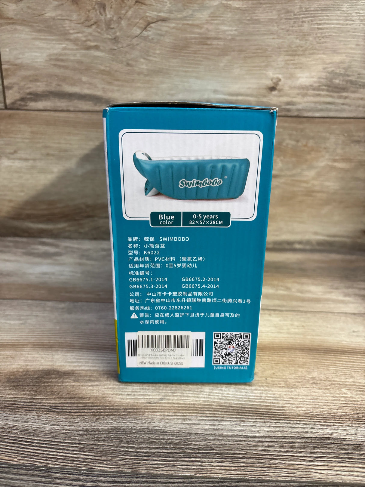 Rear view of SwimBoBo inflatable bathing tub box showing blue tub photo and size 0–5 years (82 x 57 x 28 cm) on wood surface