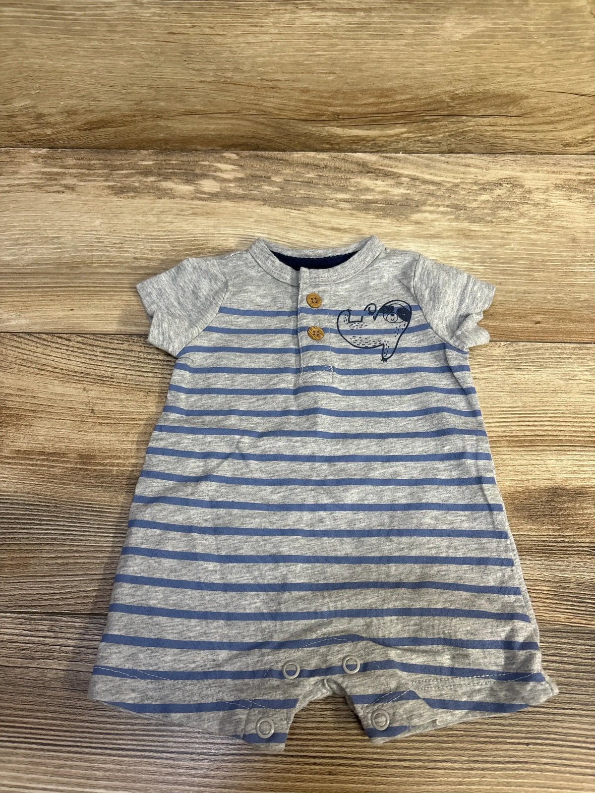 Top-down view of grey and blue striped Henley romper with two buttons, whale chest print, and snap crotch on wood floor