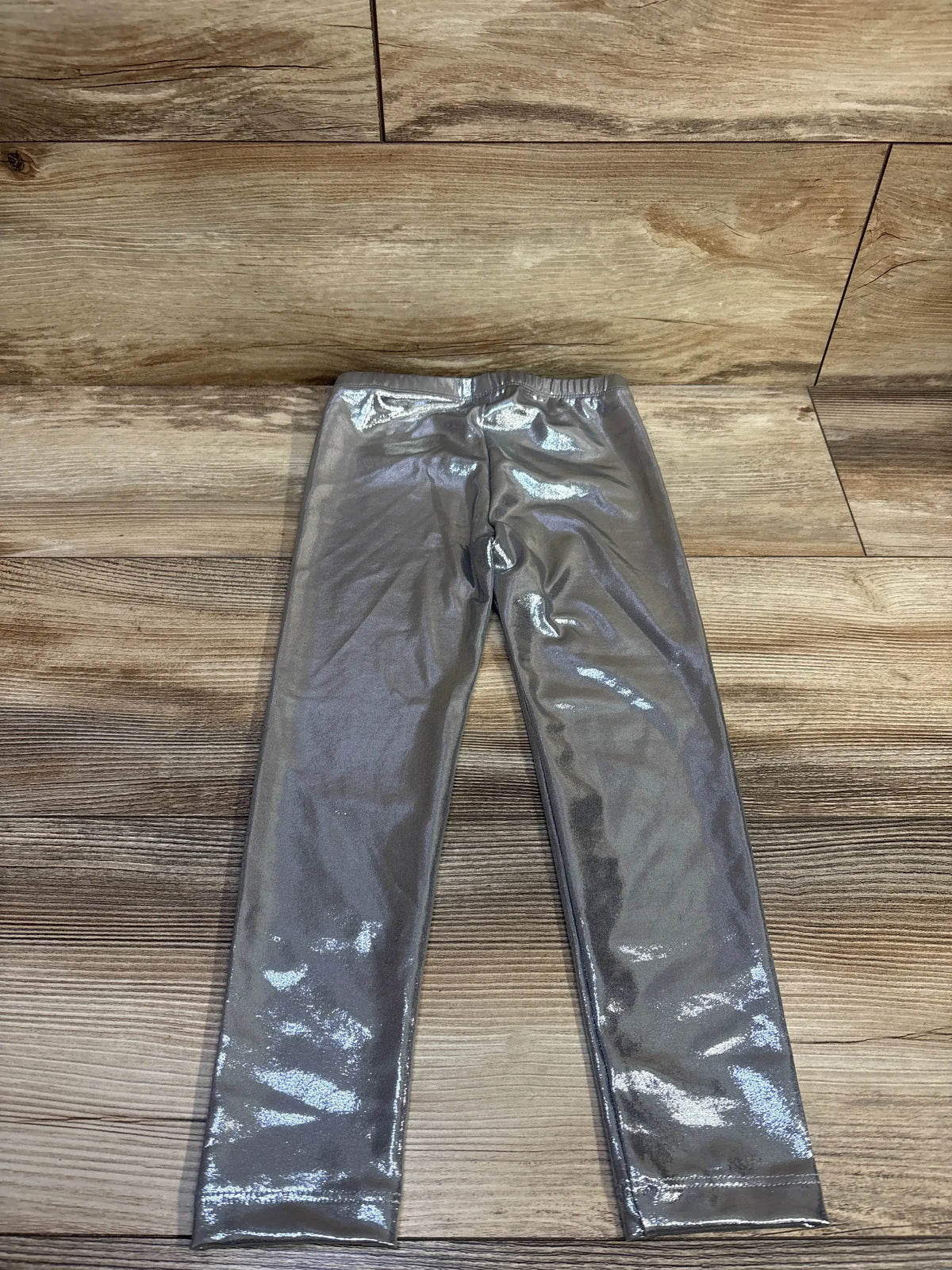 Flat-lay of Old Navy metallic silver toddler leggings (4T) showing shiny finish and elastic waistband on wood background