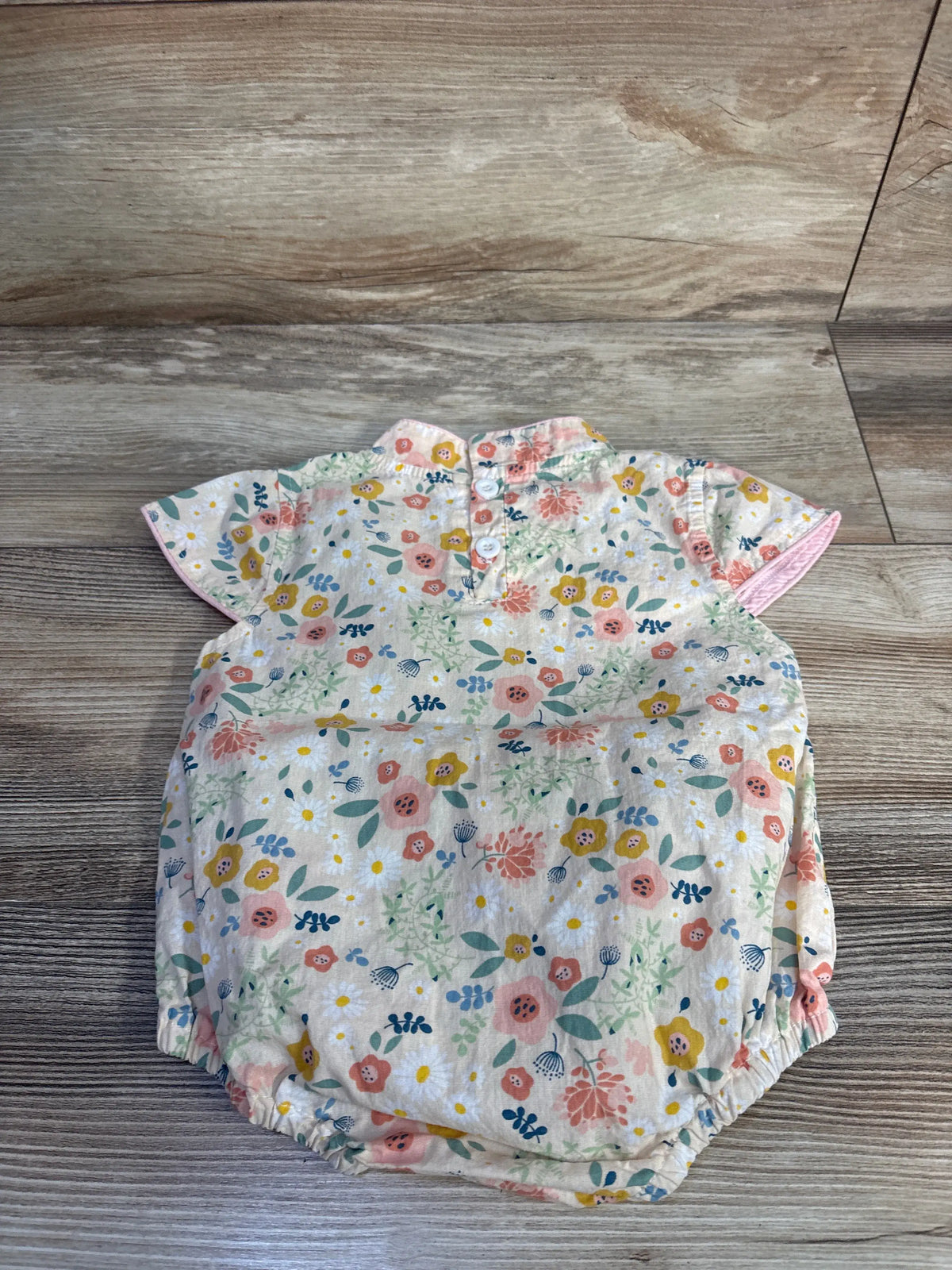 Flat-lay back of cream kimono-style floral romper with back buttons, short sleeves and elastic leg openings on wood background