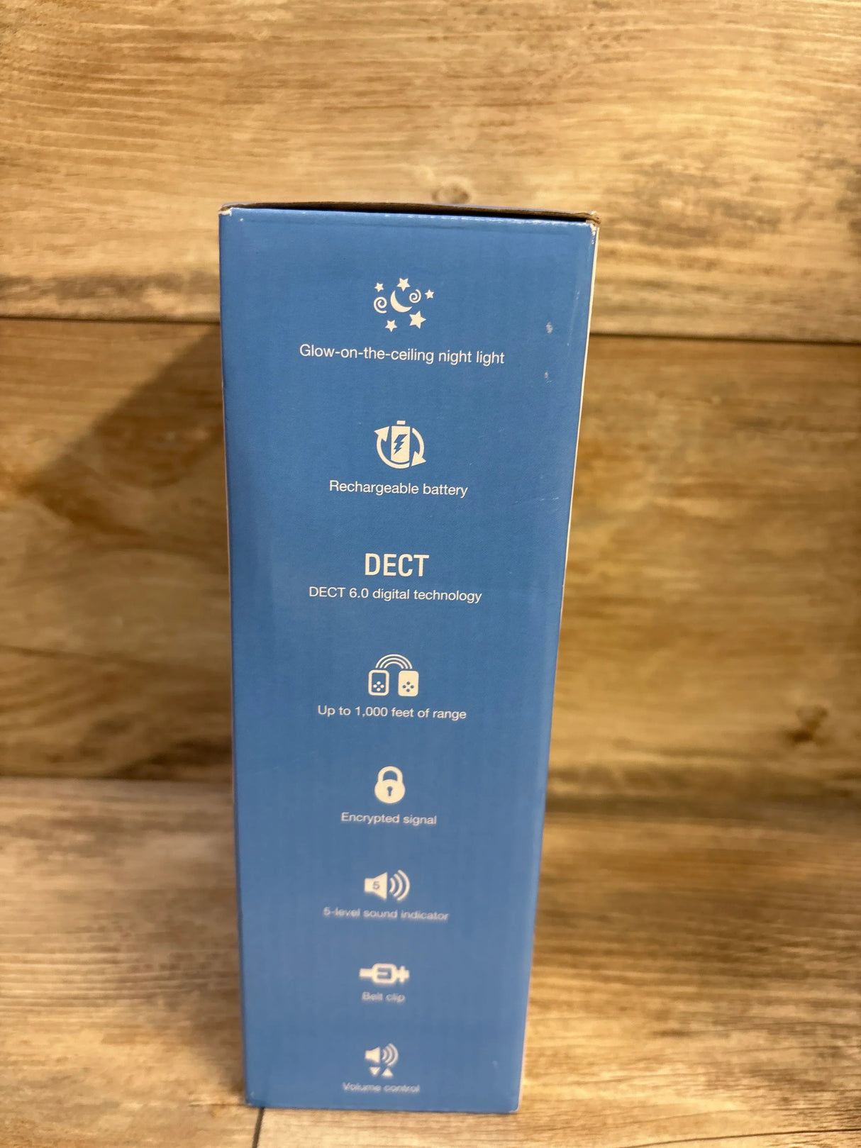 Side of V-Tech TM8112 box showing glow-on-ceiling night light, rechargeable battery and DECT 6.0 features; wooden background