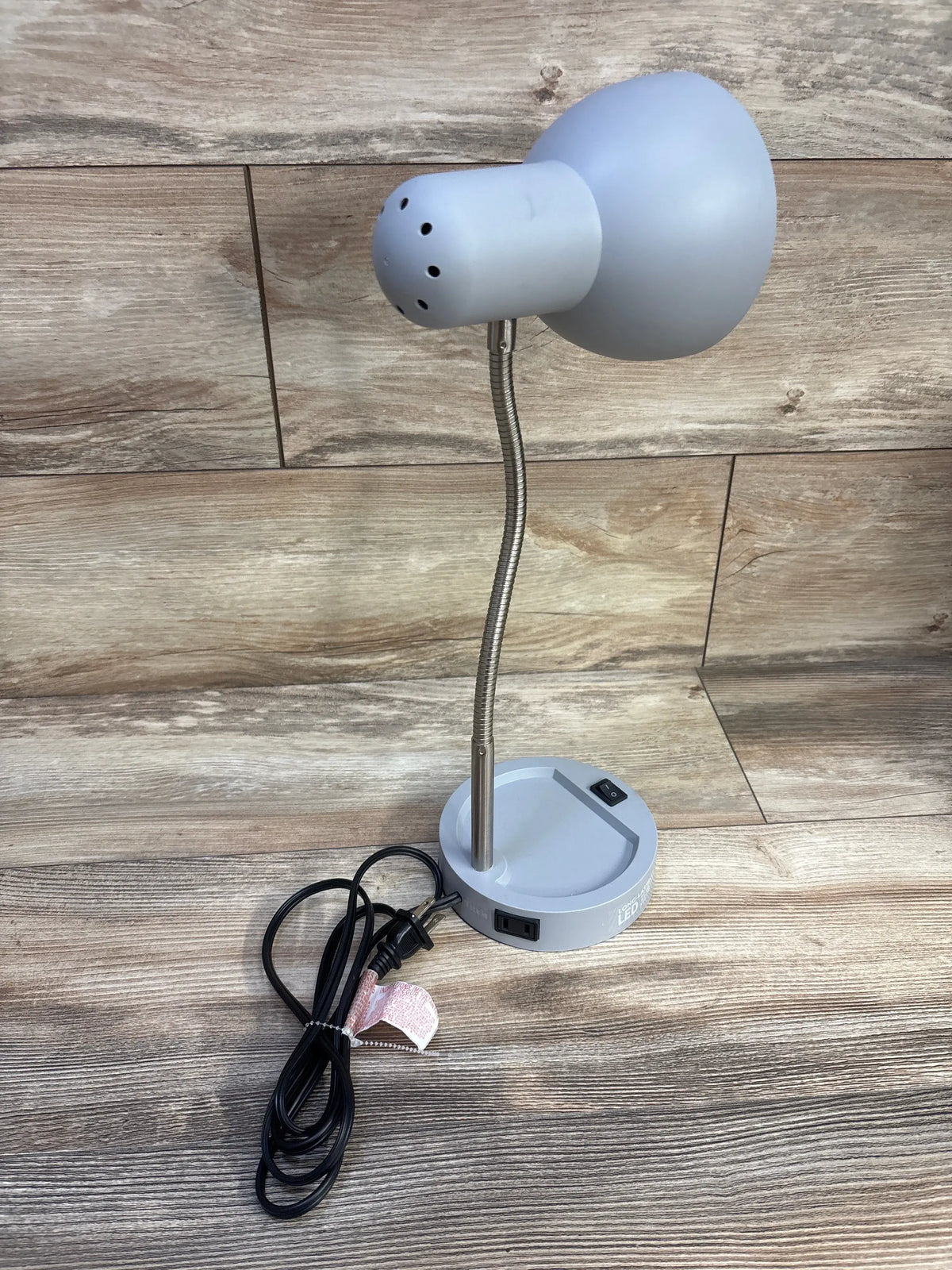 Angled view of Mainstays LED Desk Lamp with Catch-All Base, Grey showing flexible metal gooseneck and catch-all base on wood
