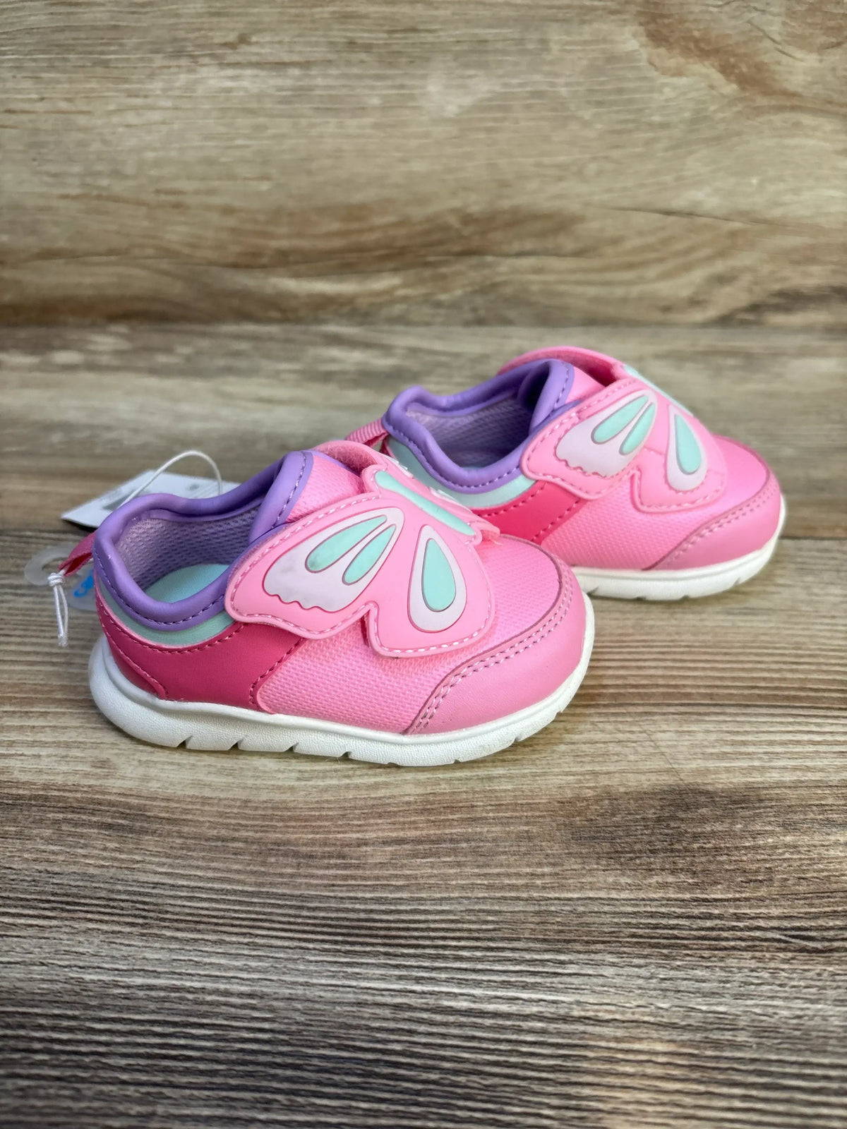 Pink toddler shoes with butterfly wing velcro straps on wood background