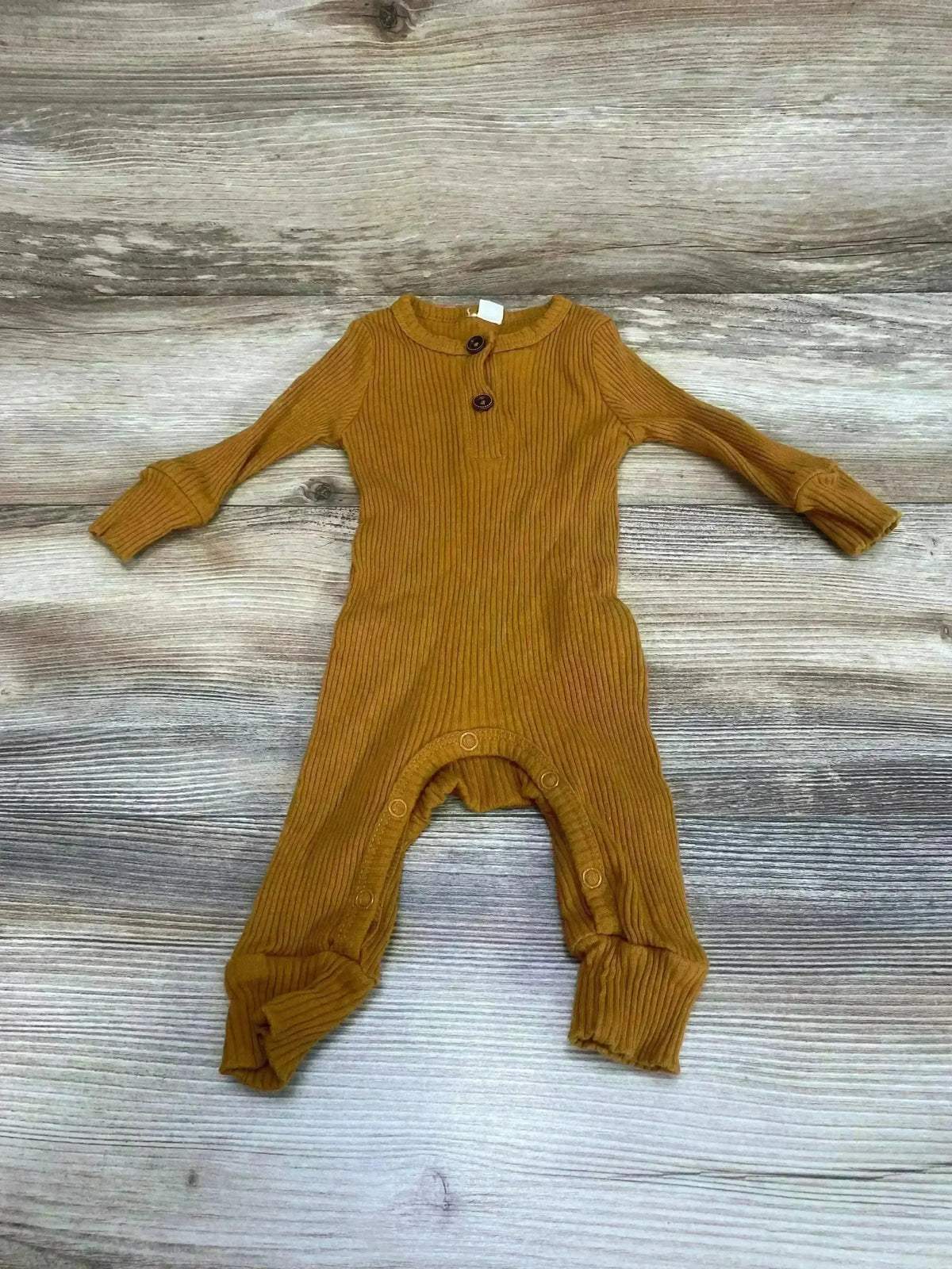Top-down view of ribbed henley coverall, brown (3M), showing two-button henley neckline, snap crotch and fold-over cuffs on wood background