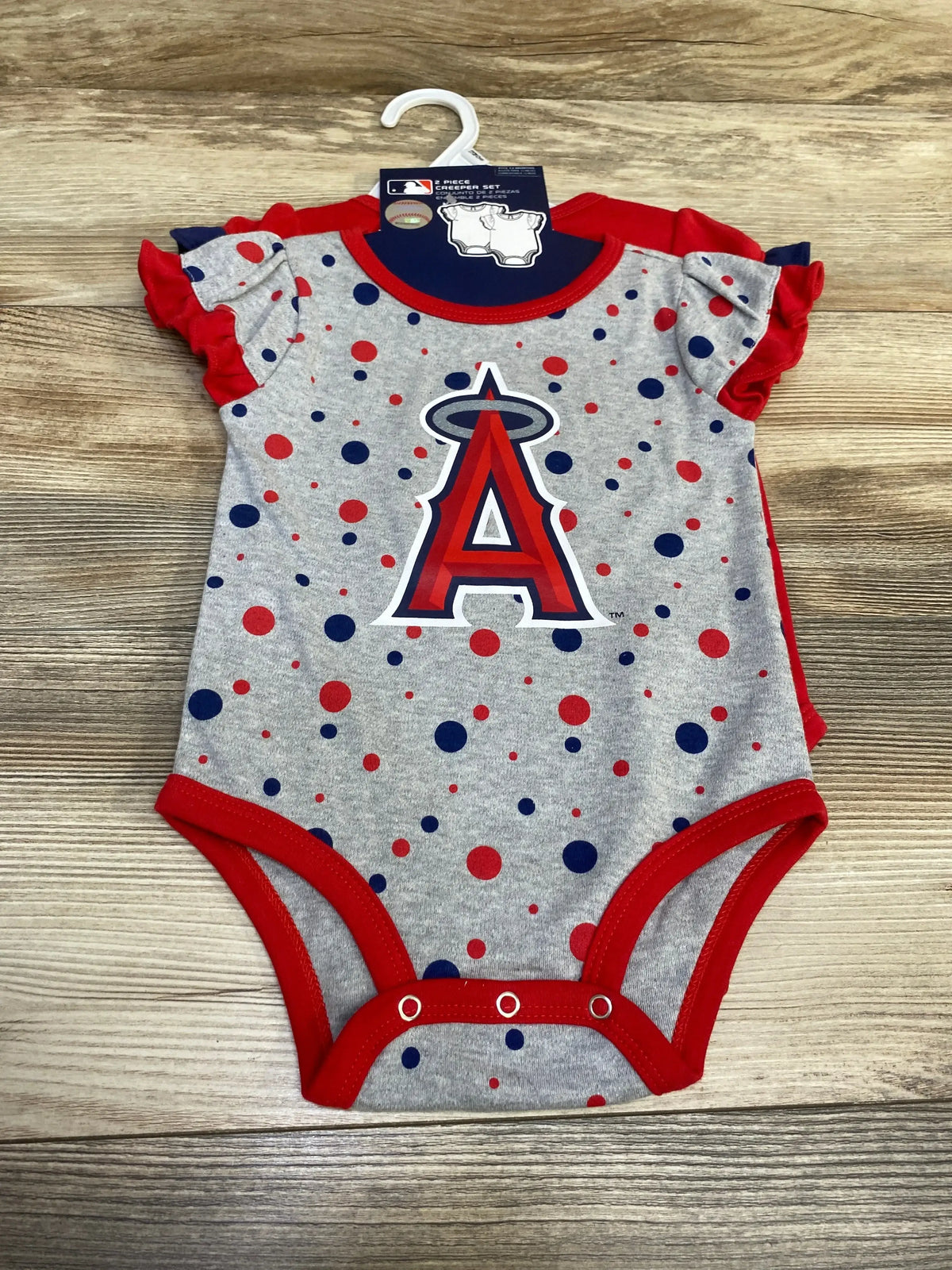 Flat-lay front of Los Angeles Angels baby onesie (2-piece, 12 months) showcasing team A logo, red ruffle sleeves, and polka dots on wood background