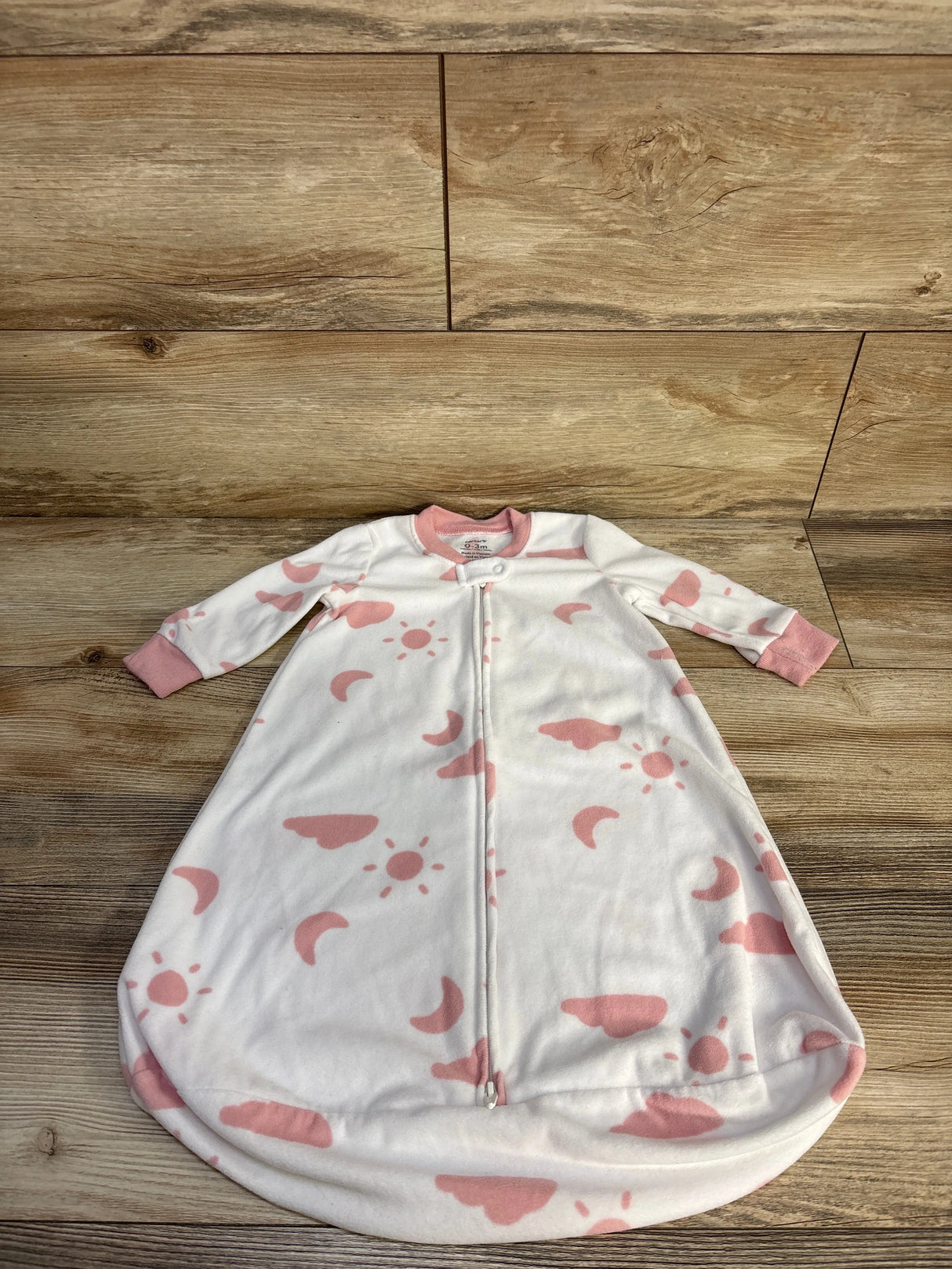 Flat front view of Carter’s white 0-3M sleep sack with pink sun, moon, and cloud print, center zipper and pink cuffs on wood background