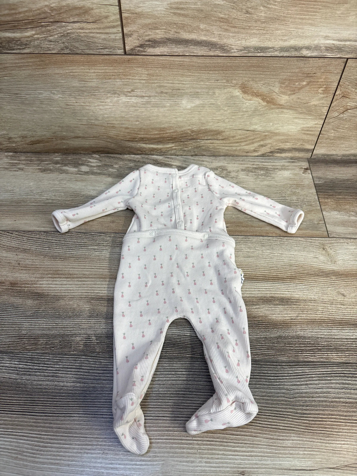 Top view of Maniere ribbed footie sleeper in ivory showcasing covered feet and long sleeves on a wood-look floor