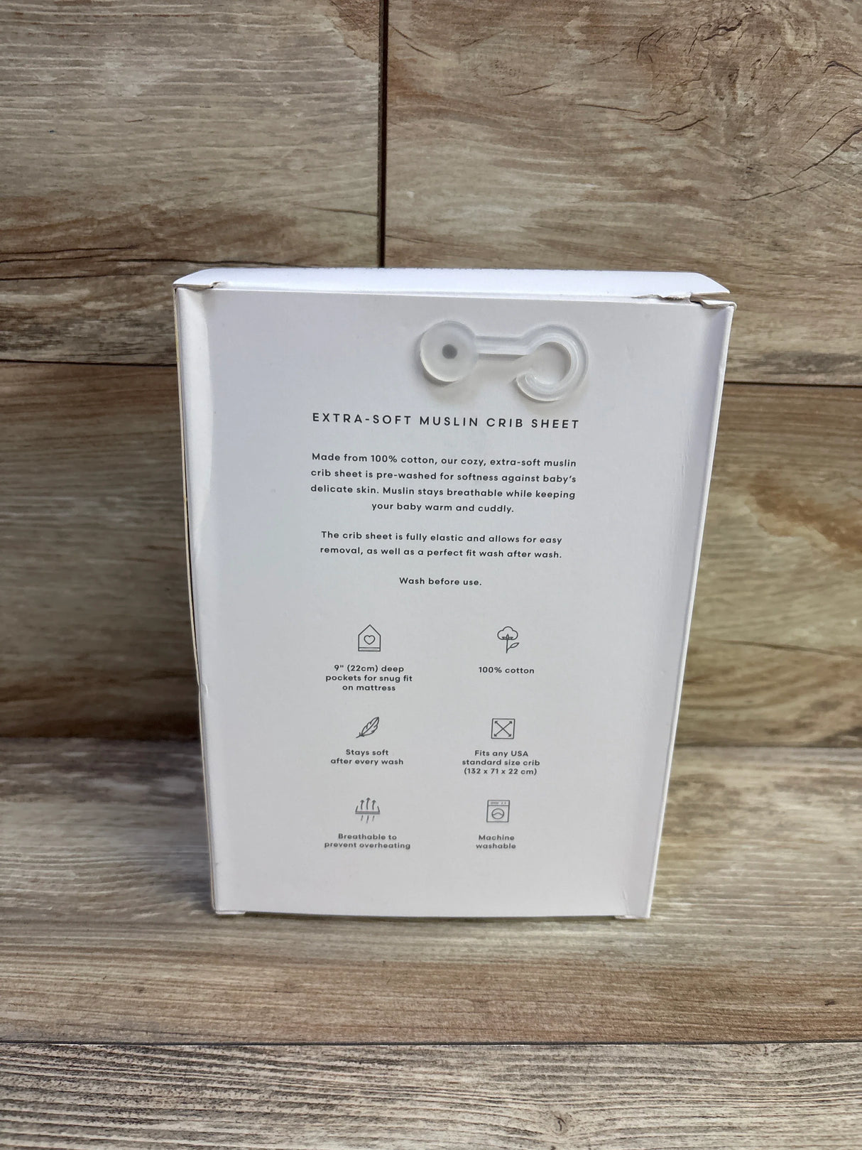 Rear of Mushie extra-soft muslin mini crib sheet box showing product features and care icons, natural stripe, 28x52, wood background