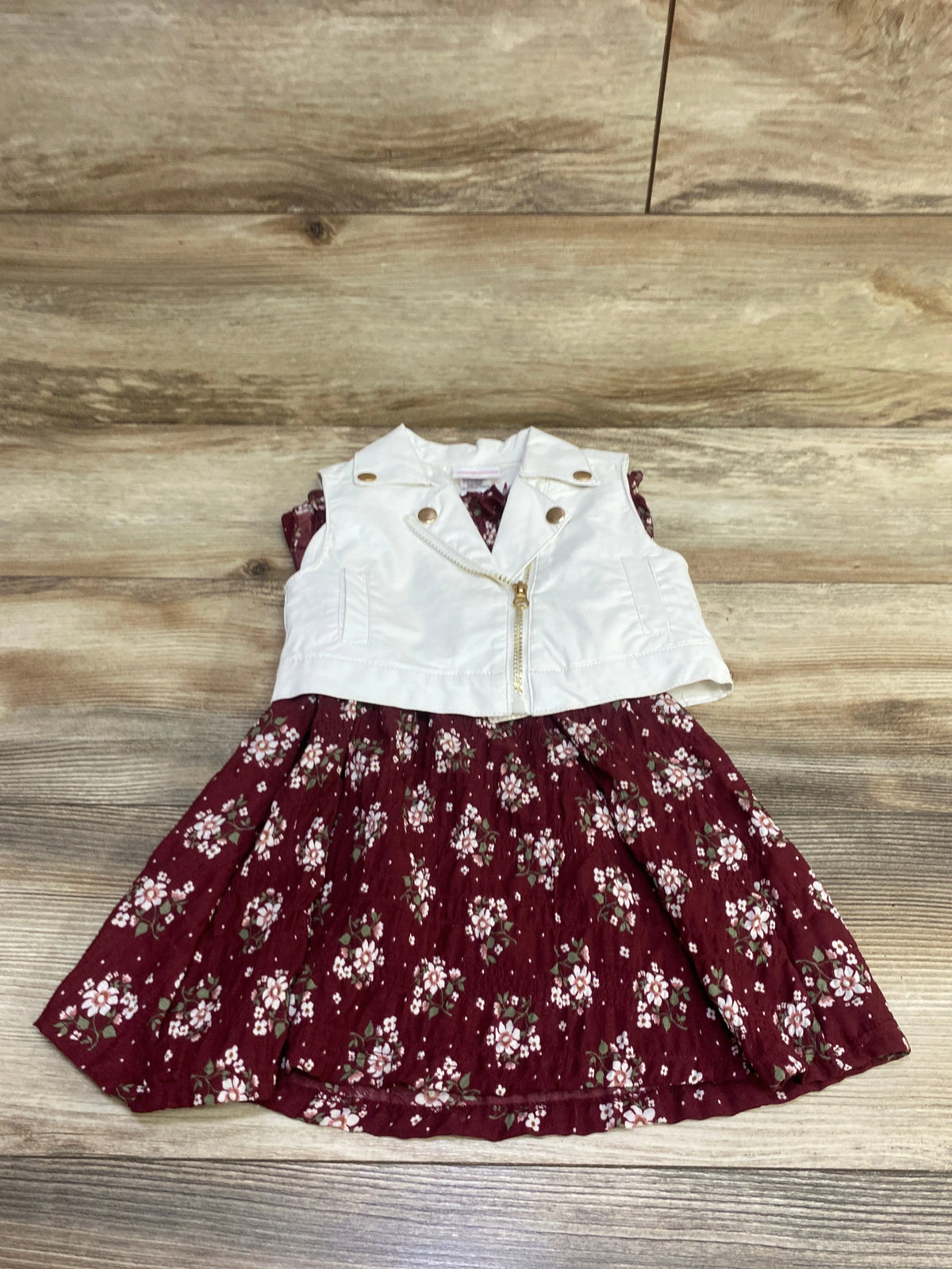 Front view of Little Lass 2-piece faux leather vest and floral dress set in white and burgundy on a wood background