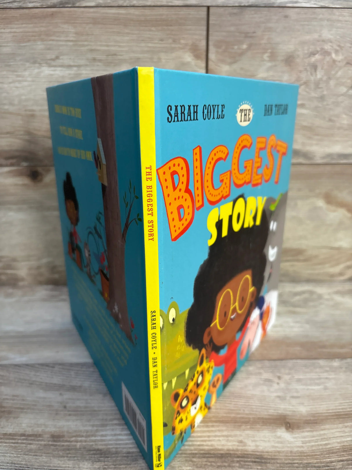 Children’s book The Biggest Story with colorful cover, child and animal illustrations, on wood surface