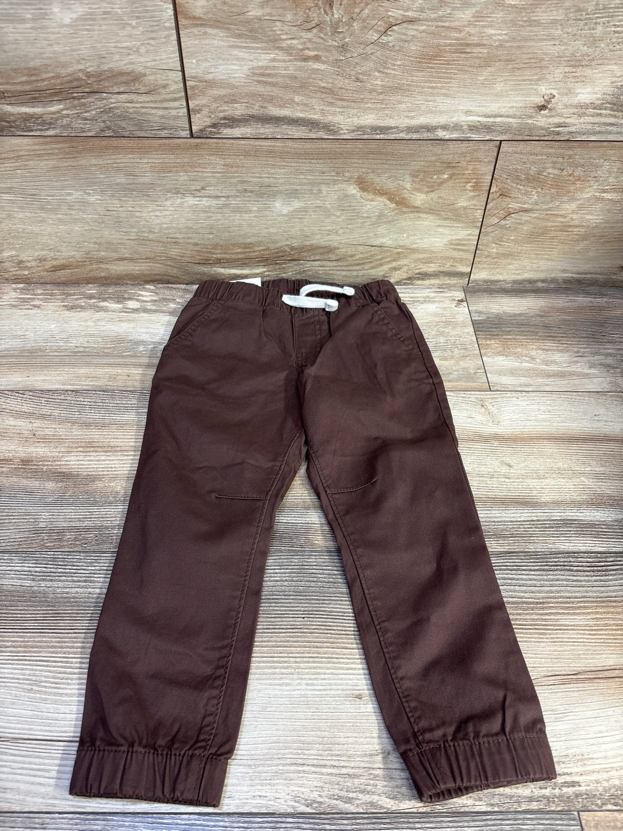 Front flat lay of brown Cat & Jack toddler drawstring joggers size 3T showing white drawstring, elastic waistband and elastic cuffs on wood background