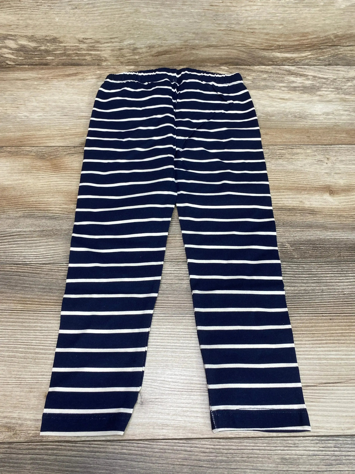 Flat lay of NWT Baby Gap leggings in navy blue with white horizontal stripes and elastic waistband on wood plank floor