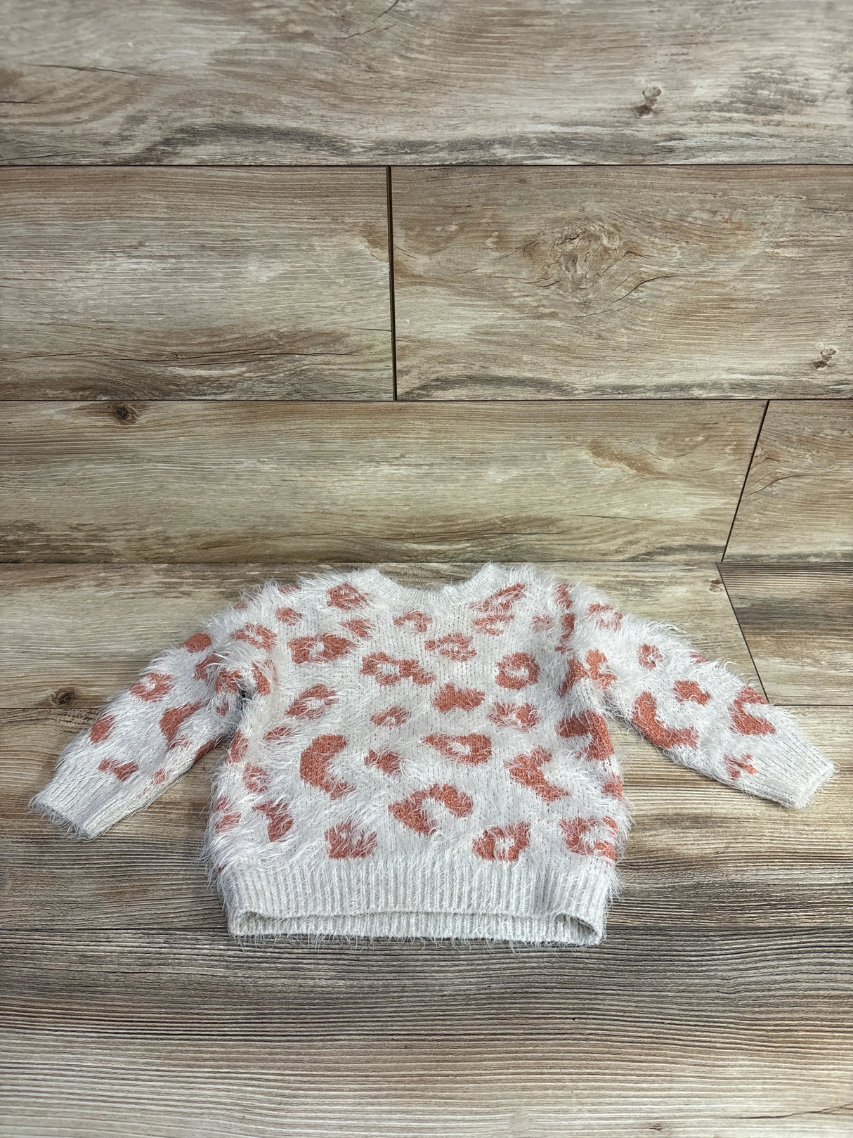 White fuzzy toddler sweater with orange leopard print pattern on wooden floor