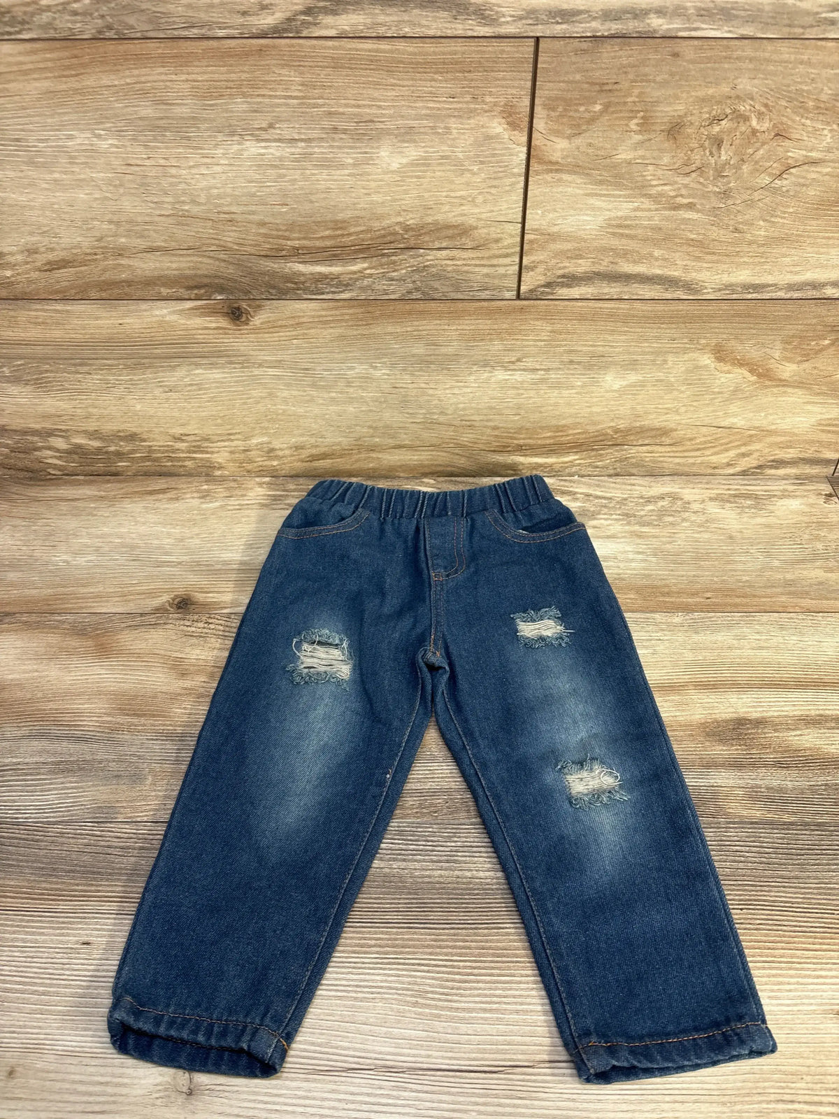 Flat lay of blue toddler distressed pull-on jeans size 18-24 months showcasing elastic waistband and ripped knees on wood background