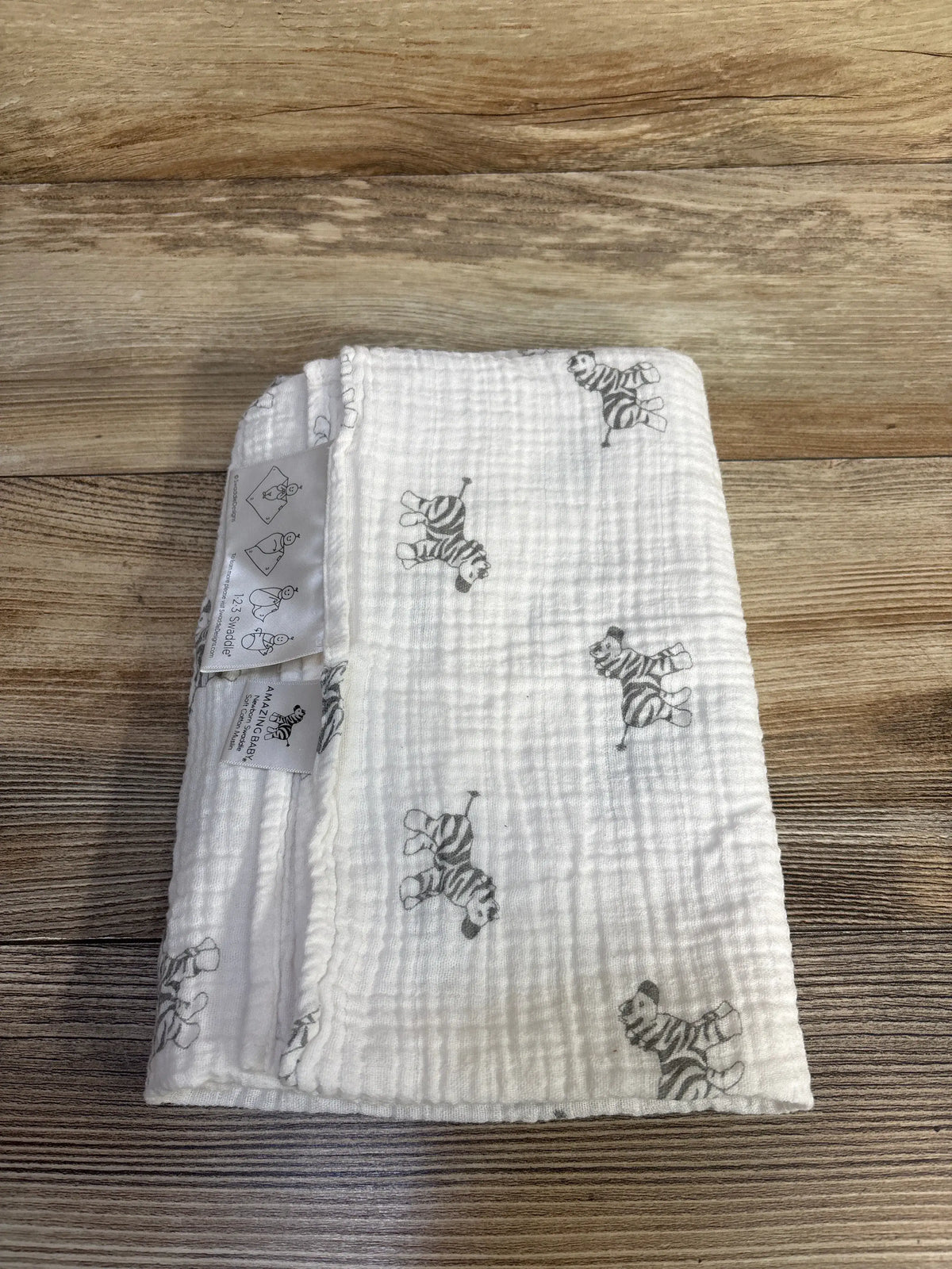Top view of Amazing Baby muslin swaddle blanket showcasing white 100% cotton fabric with zebra print on wood