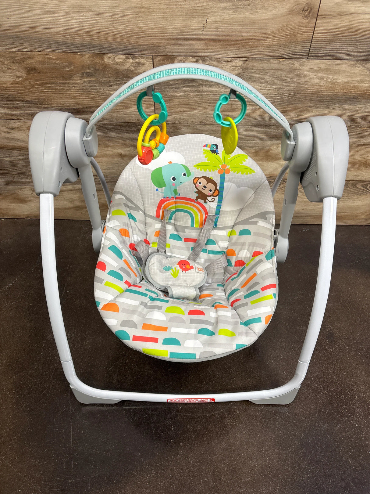 Front view of Bright Starts Playful Paradise swing showing colorful seat with elephant and monkey print and toy bar on wood